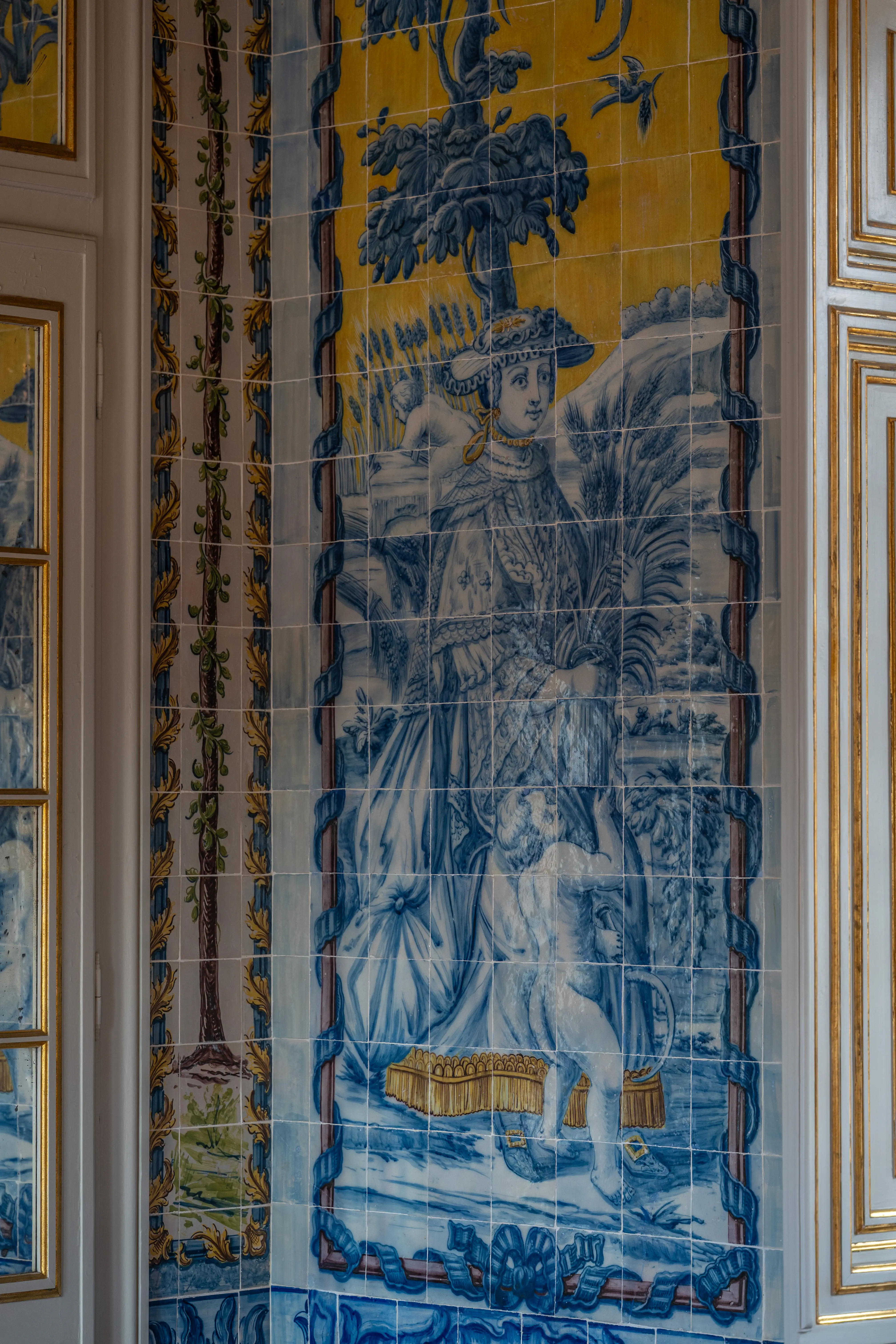 Close-up of a vintage Portuguese or Spanish azulejo tile panel showing a mythical scene with figures, a pyramid, and a phoenix, rendered in blue, yellow, and brown hues.