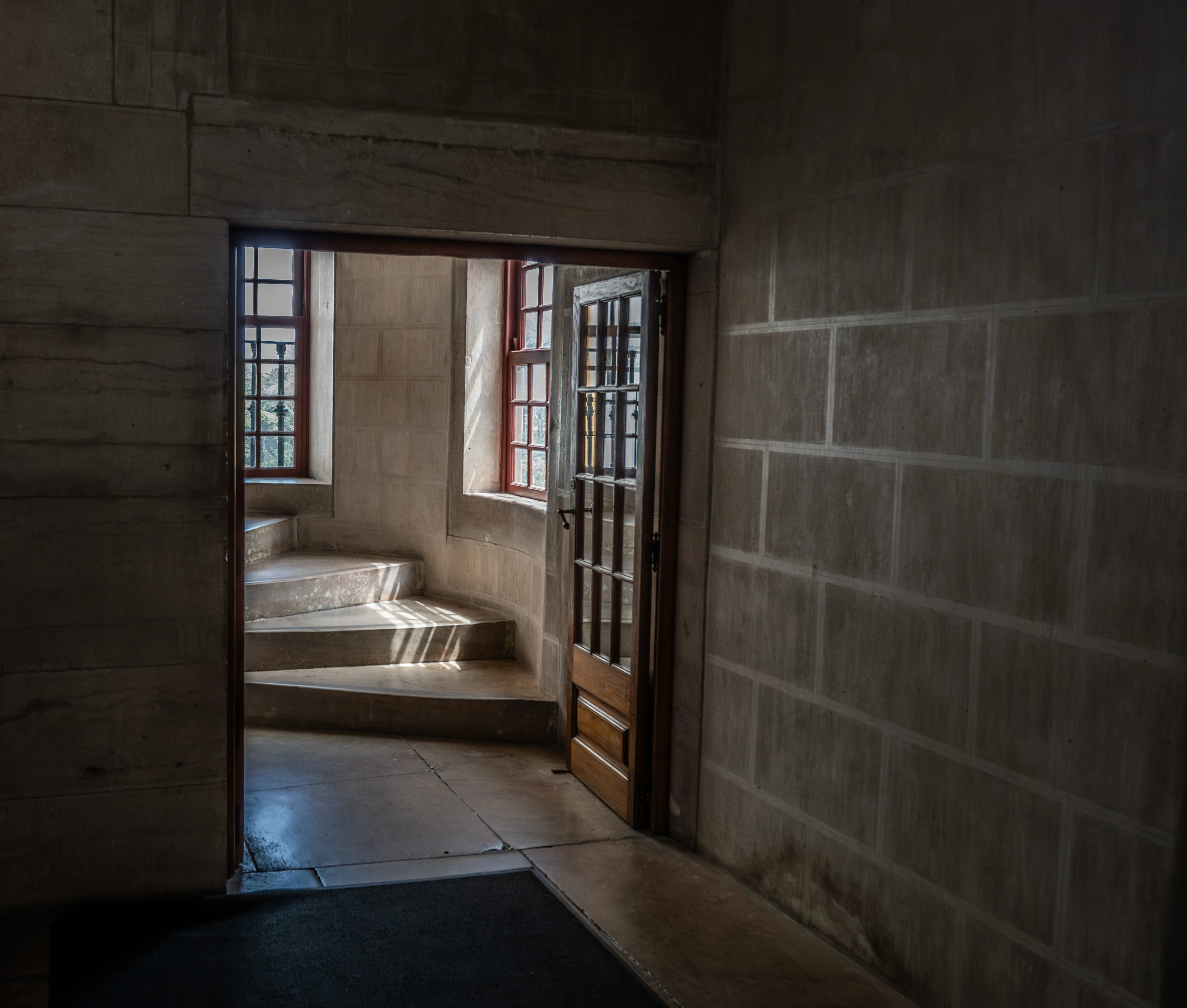 A doorway opens to reveal a stone staircase bathed in dramatic sunlight, with light casting striped shadows across the steps and floor.