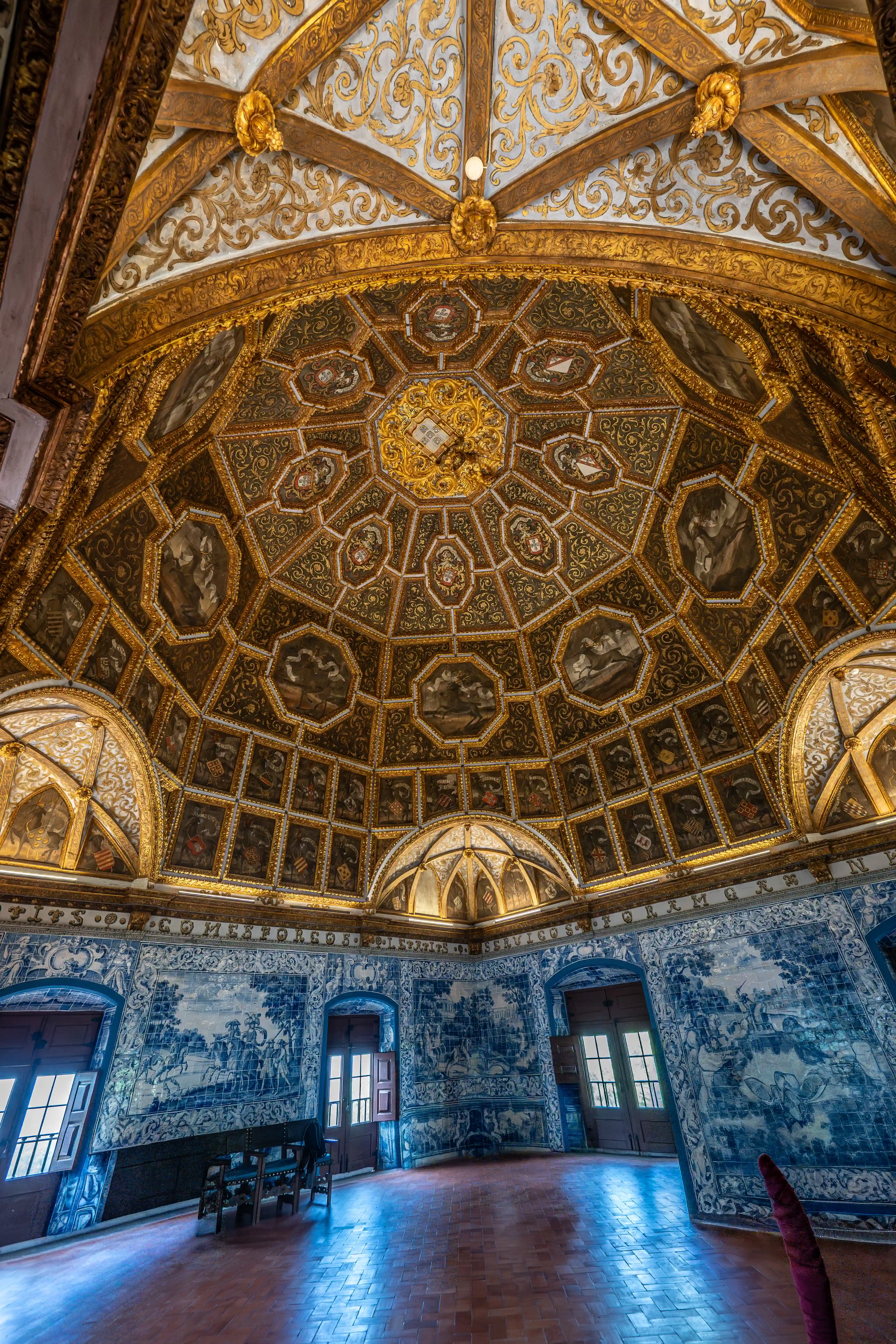 Interior view of a room with a large, ornate golden dome and walls covered in blue and white decorative tiles, with several people looking around.