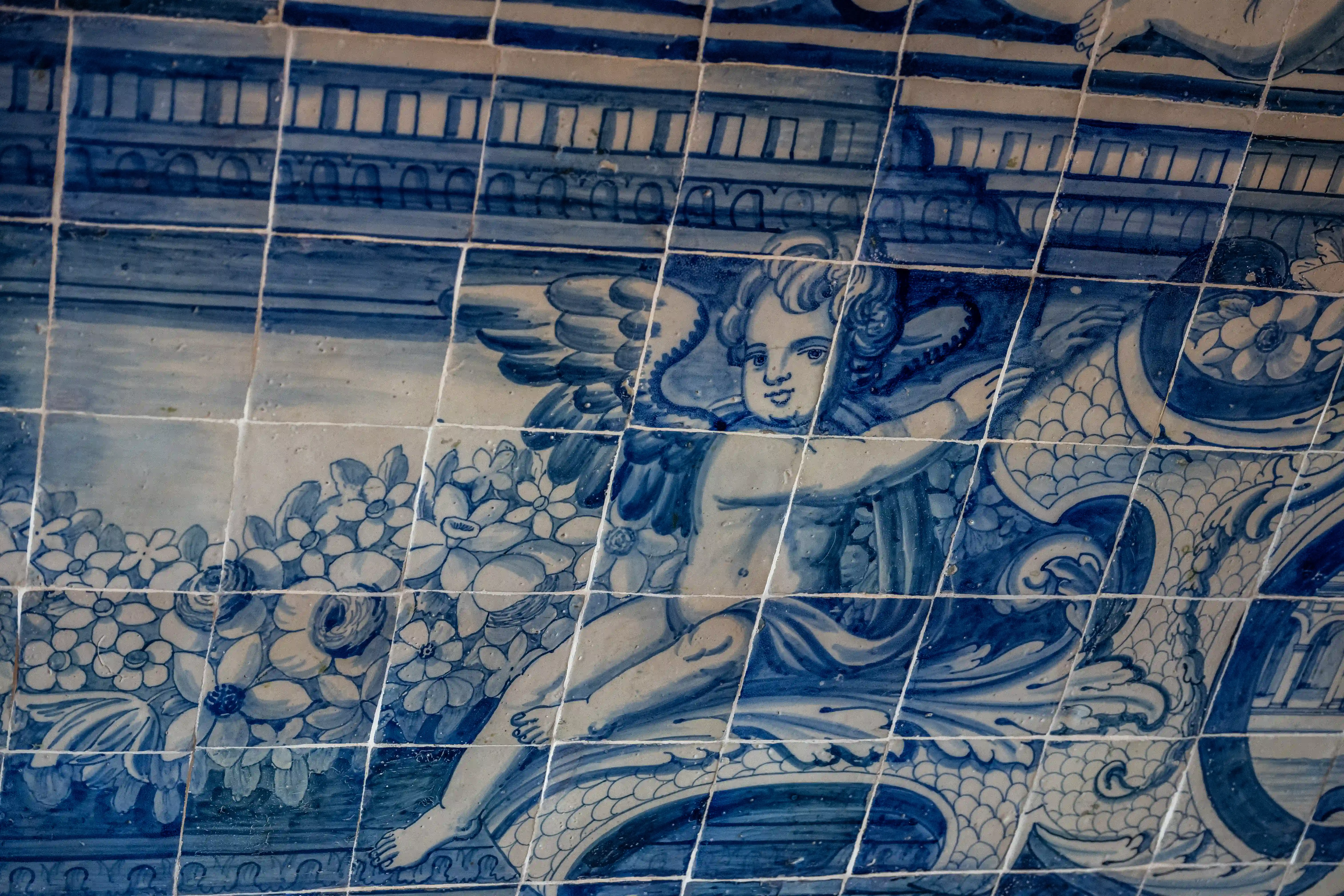 A blue and white tiled panel featuring a painted cherub surrounded by flowers and decorative patterns.