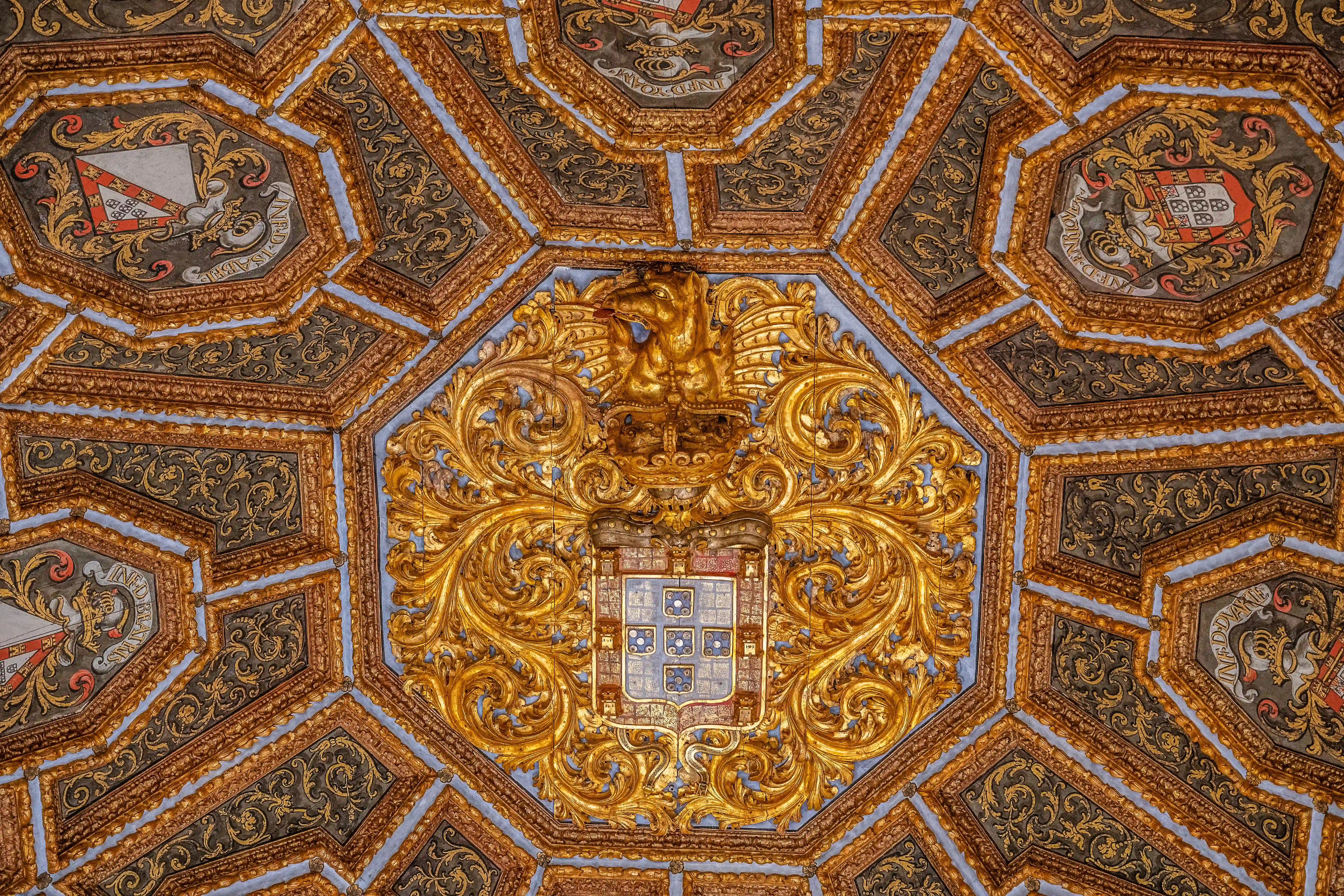 Detailed view of an elaborate octagonal ceiling with gold geometric patterns, heraldic crests, and painted scenes of stags.