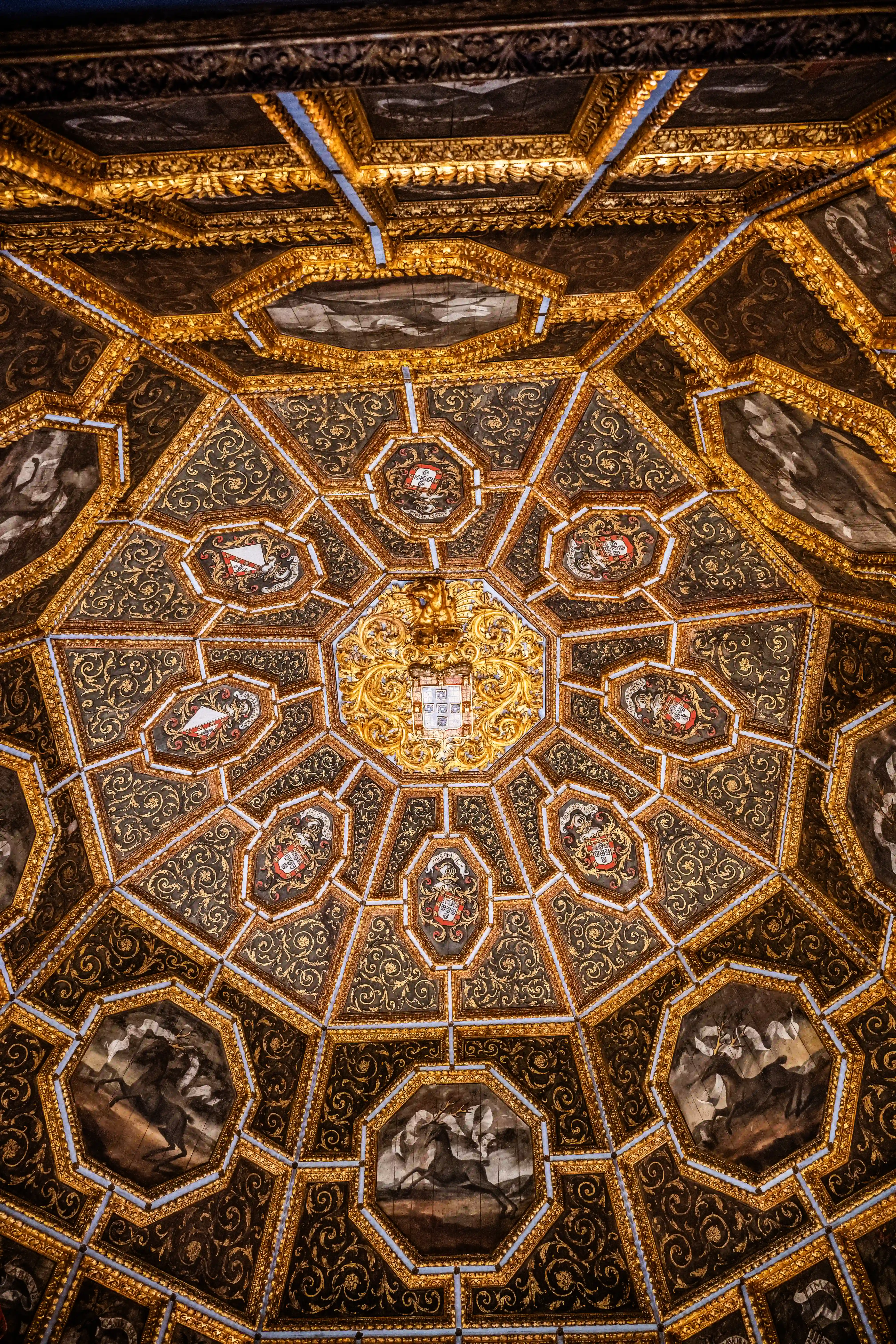 Detailed view of an elaborate octagonal ceiling with gold geometric patterns, heraldic crests, and painted scenes of stags.