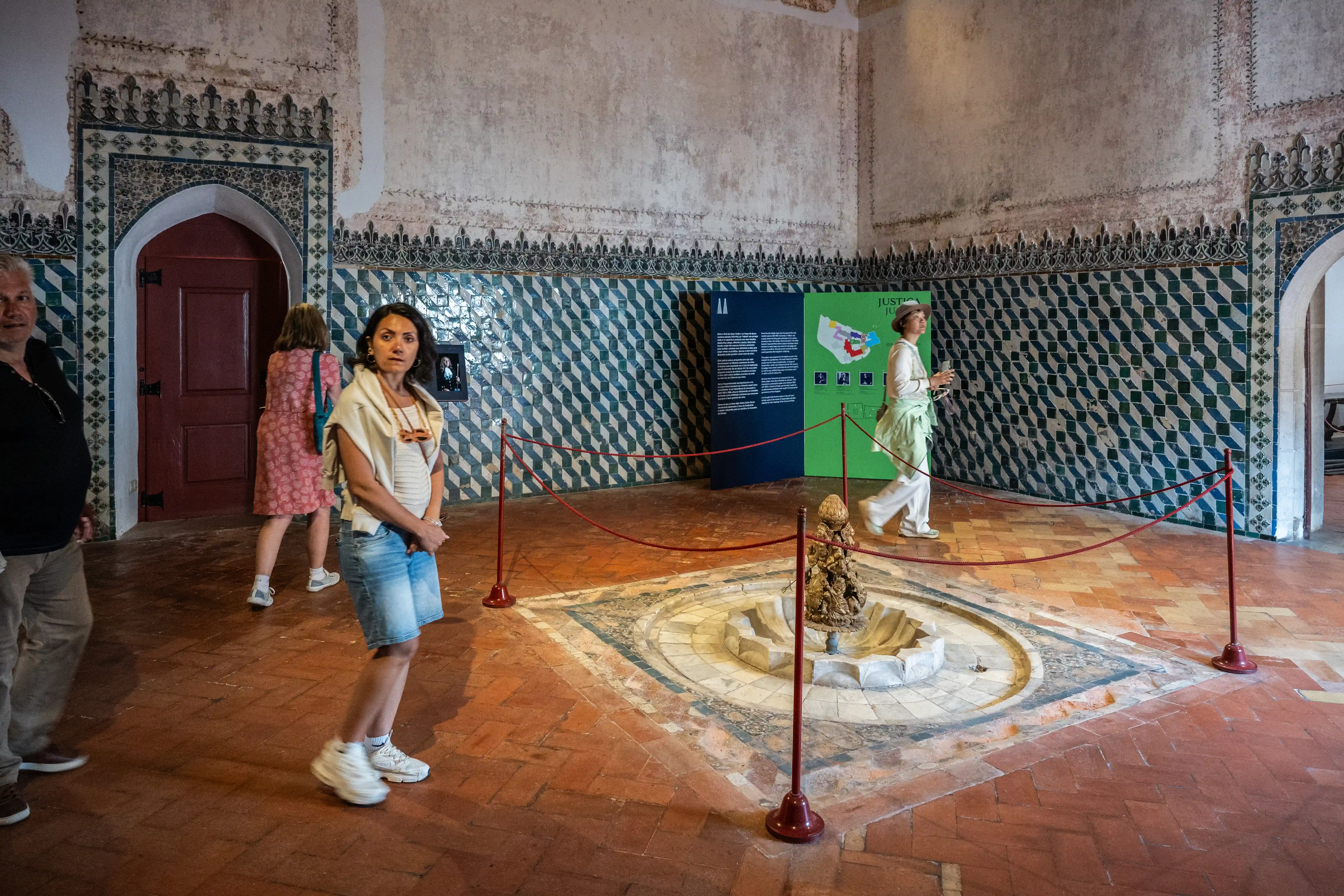 Tourists inside a building with tiled walls and a central fountain.