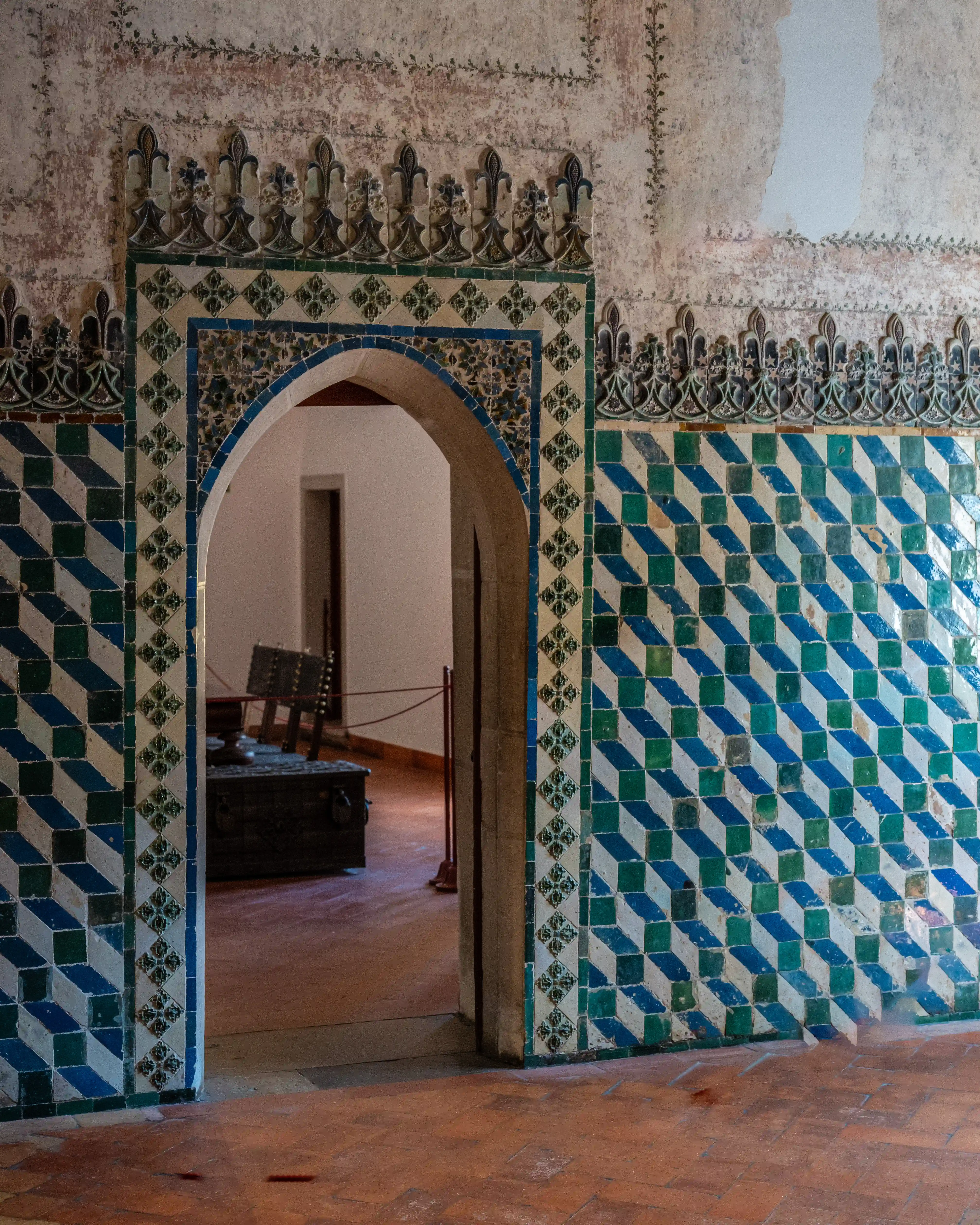 Interior view of an archway decorated with blue and green geometric azulejo tiles, leading into a room with antique furniture.