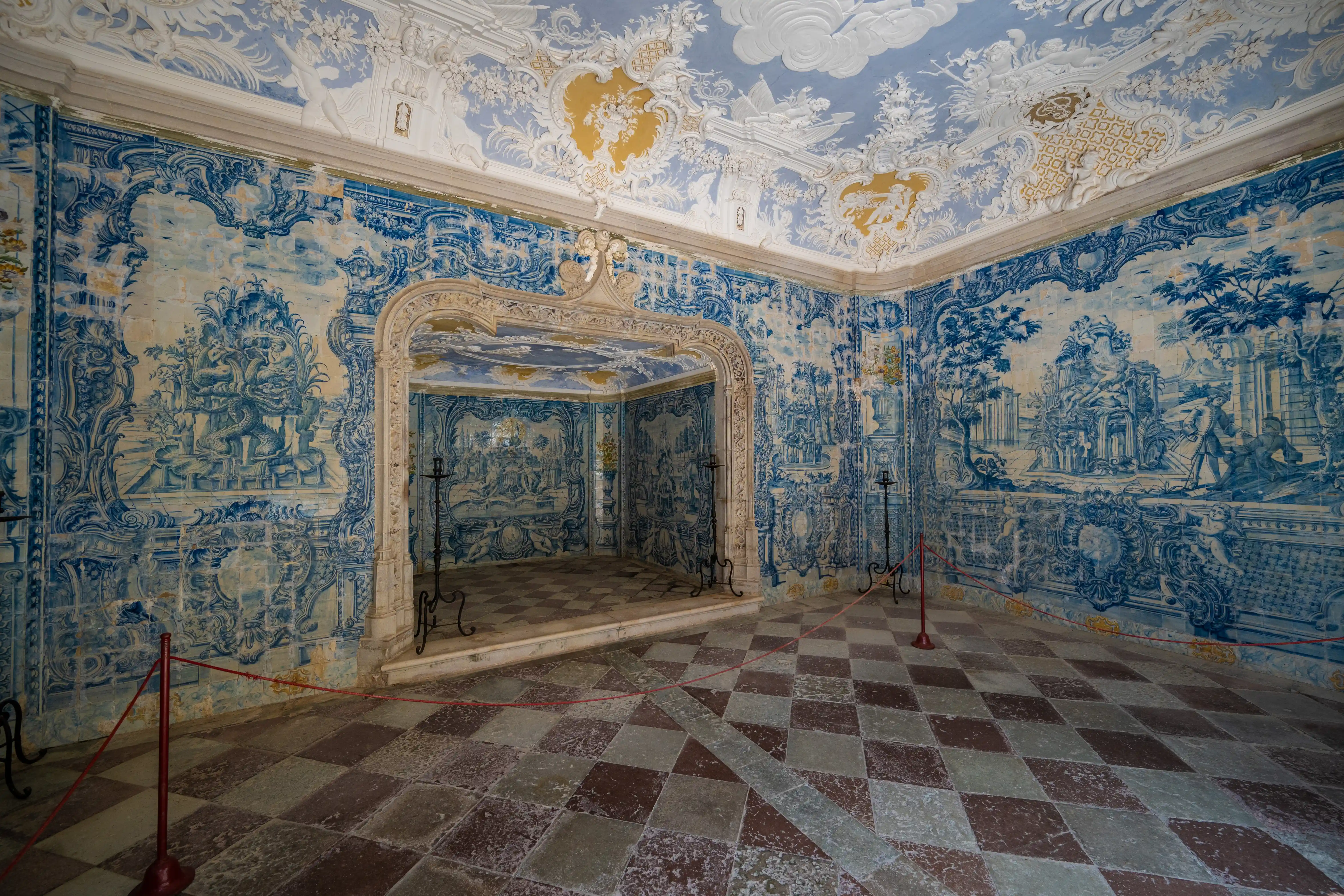 Interior view of a richly decorated room with blue and white tiled walls, a tiled alcove, ornate stuccoed ceiling, and a checkerboard floor.