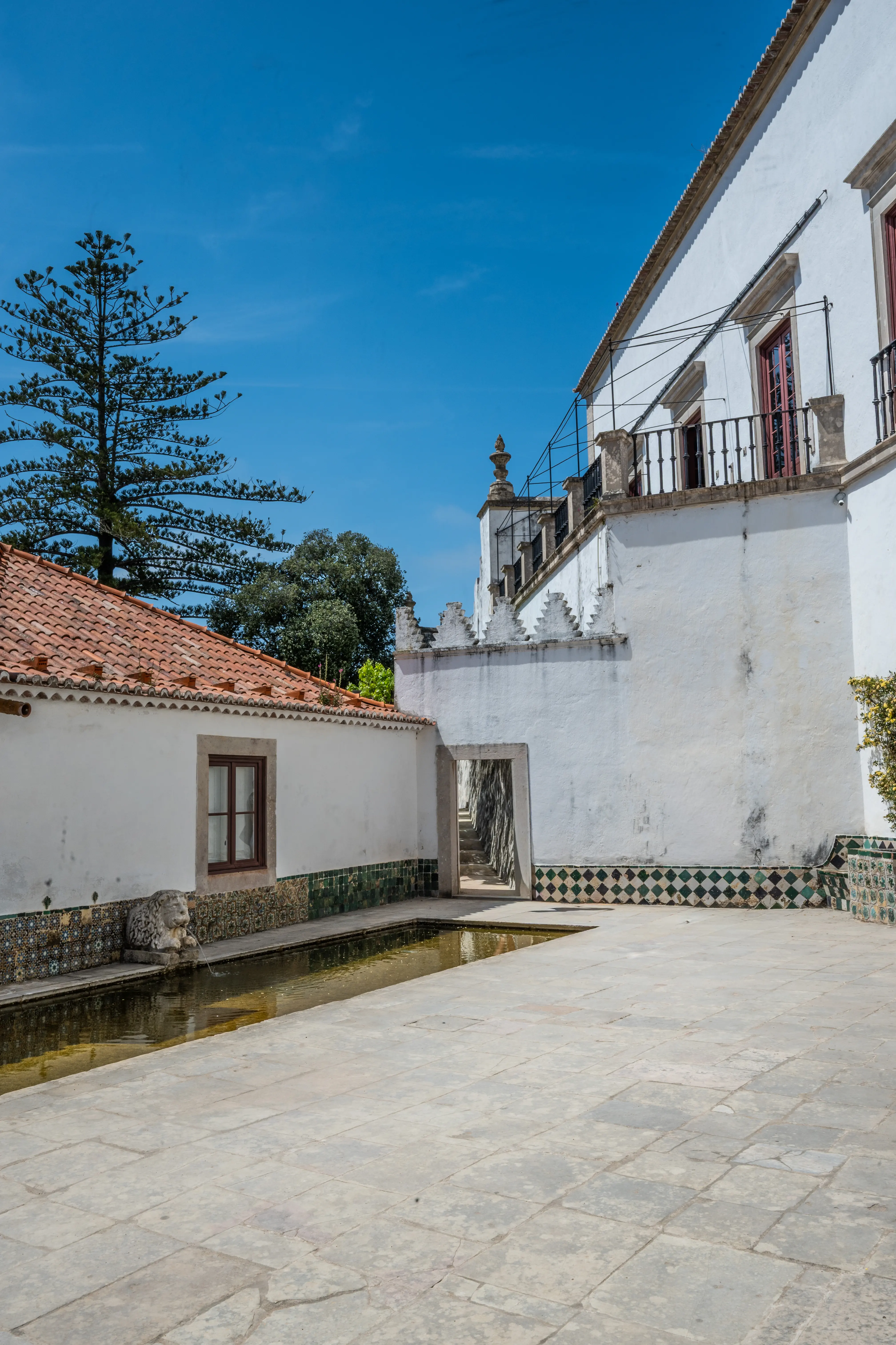 People walking in a courtyard next to a building with a tiled roof and a reflecting pool
