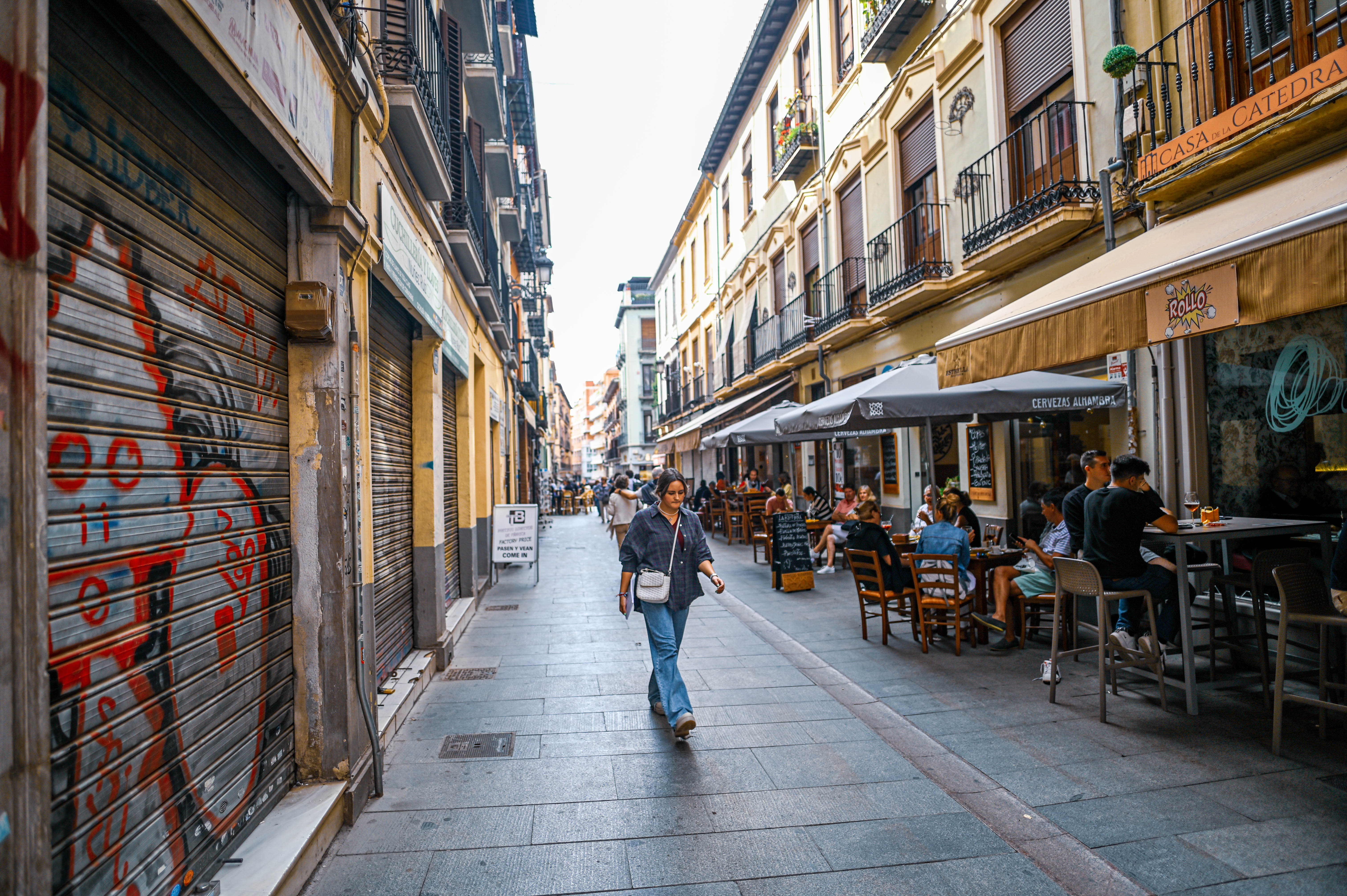 The street is lined with closed shops on the left and outdoor seating areas of cafes and restaurants on the right