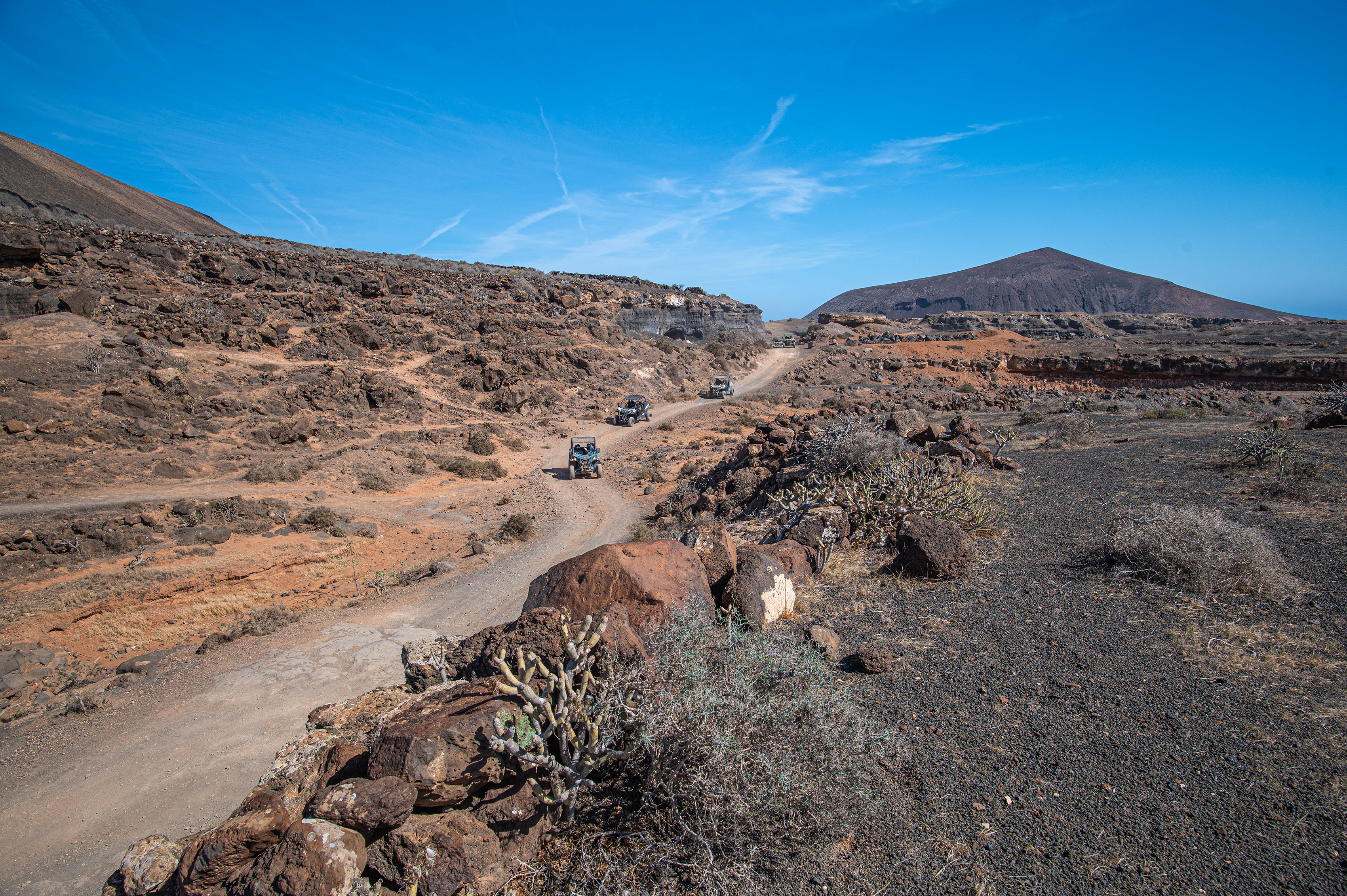 A dirt road winds through the terrain, with several off-road vehicles traveling along it
