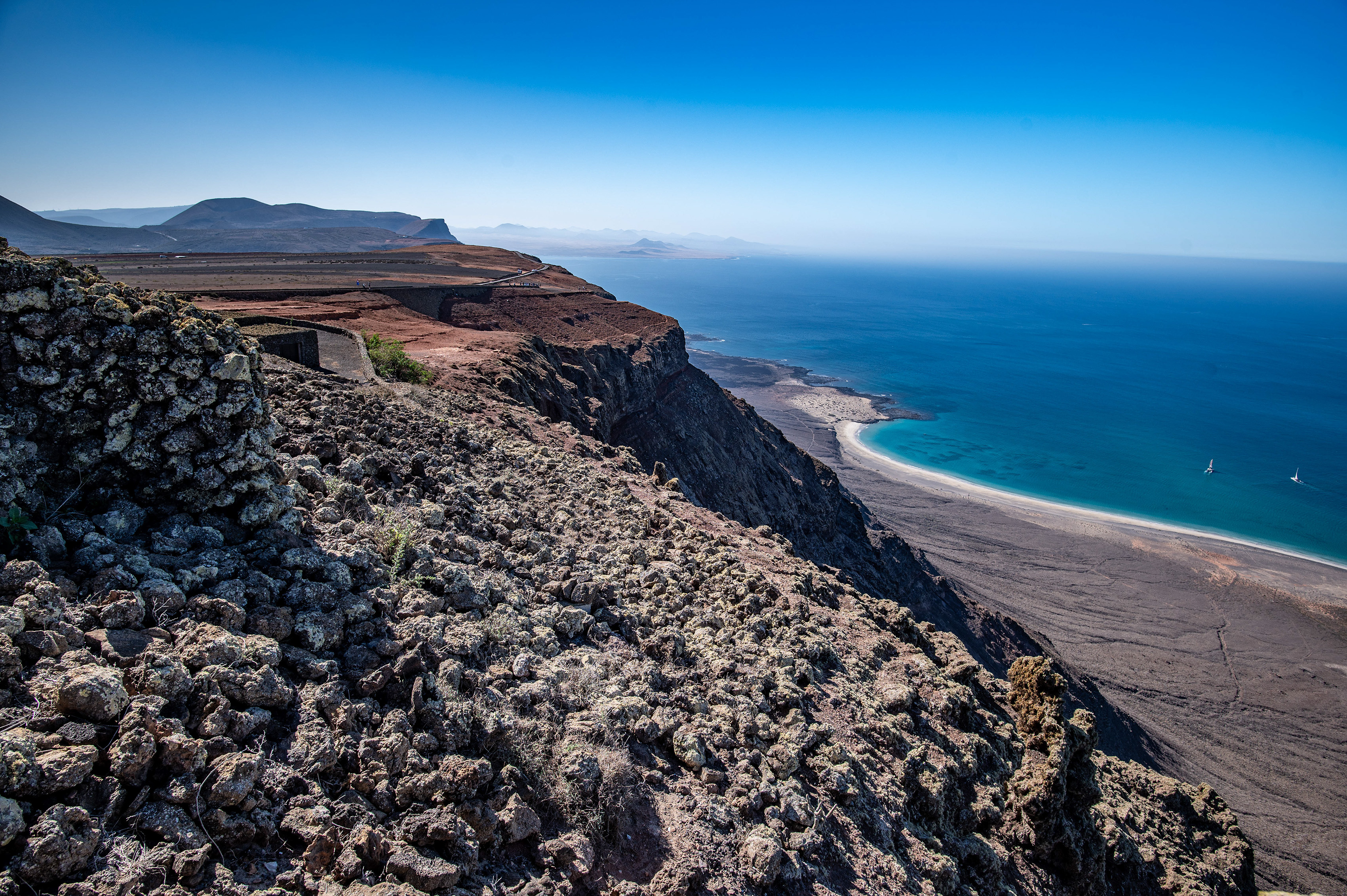 a rugged, rocky coastline with a steep cliff descending to a small, secluded beach
