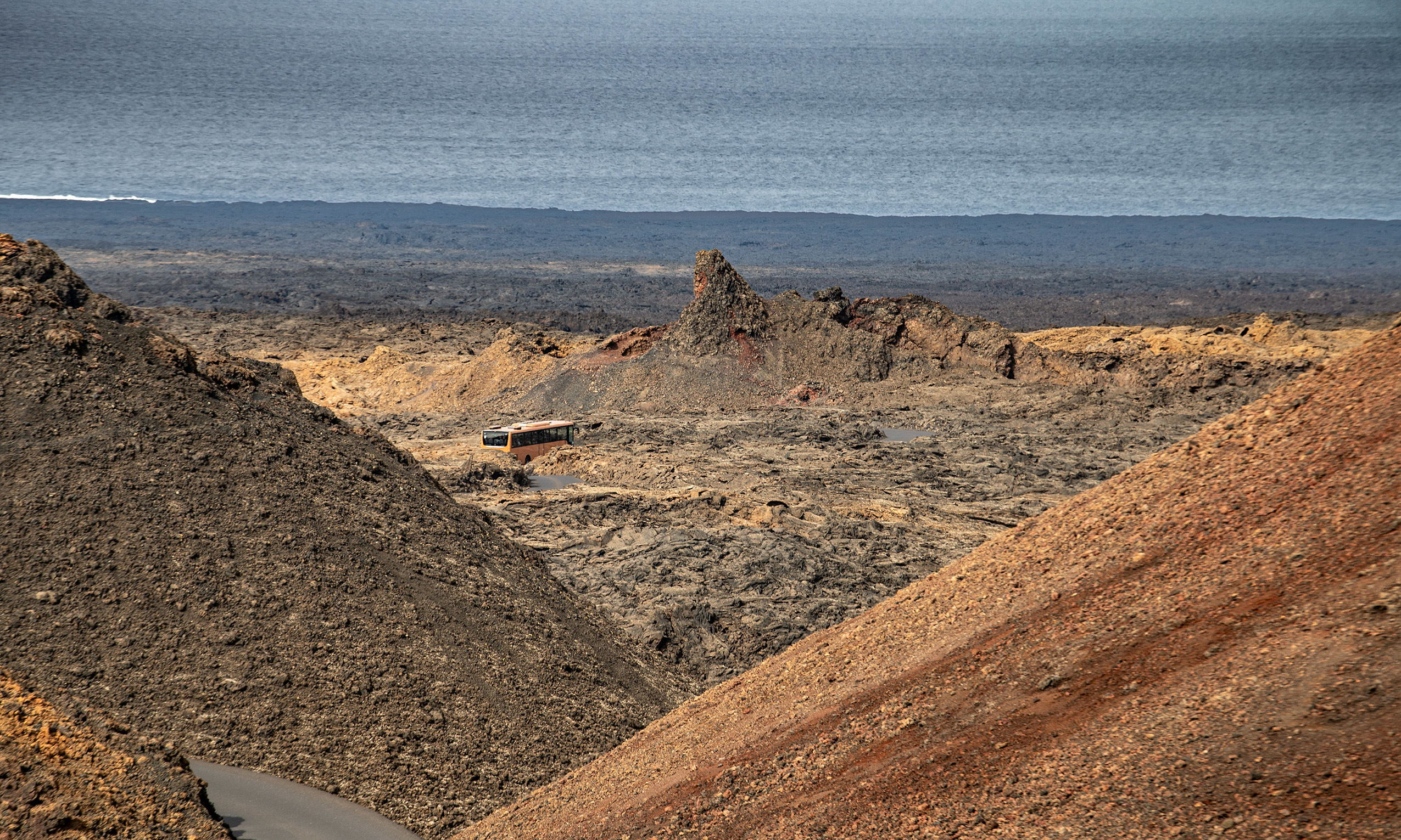 volcanic landscape with a bus traveling along a narrow, winding road