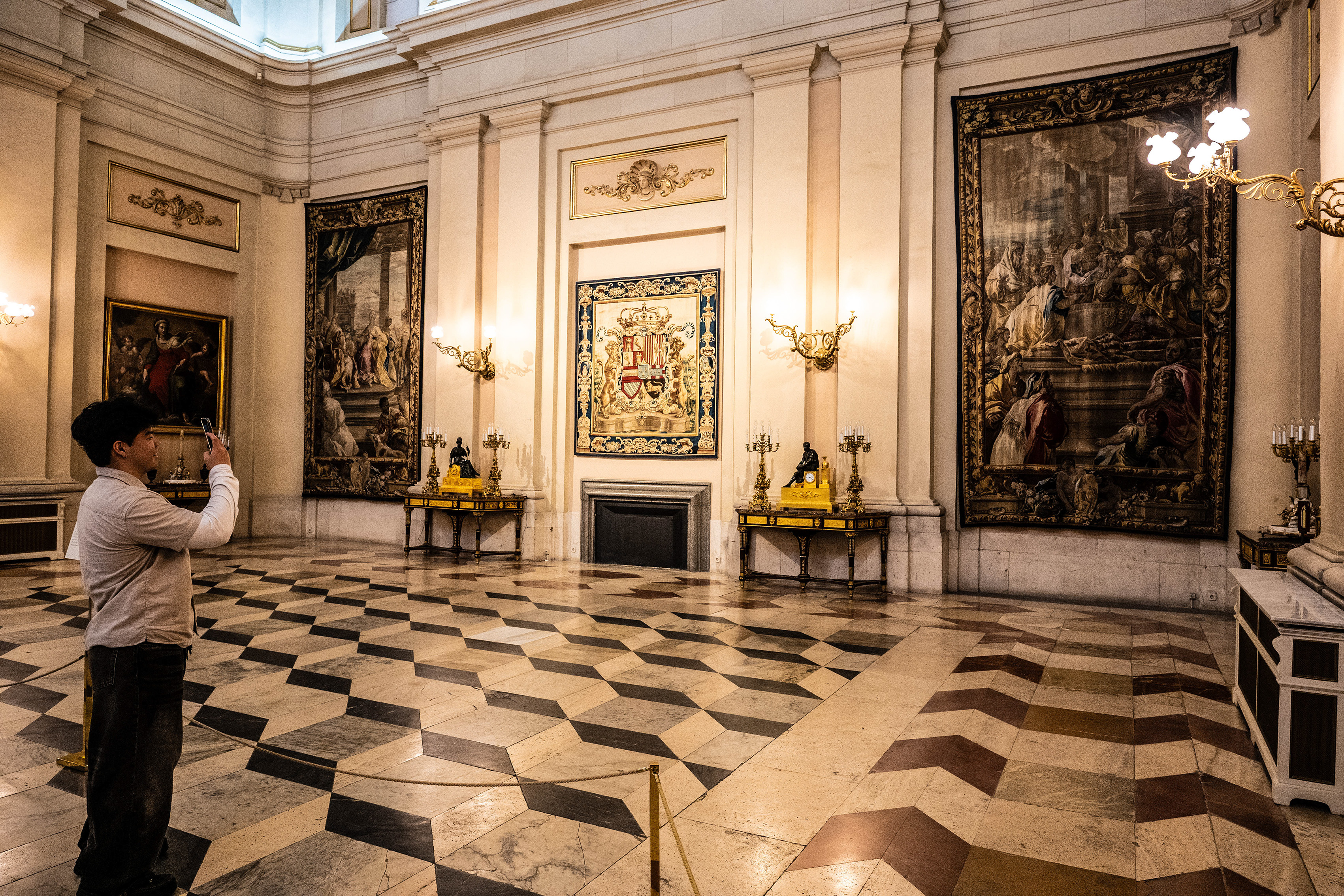 The room features intricate floor tiles, large paintings, and decorative elements such as chandeliers and candelabra