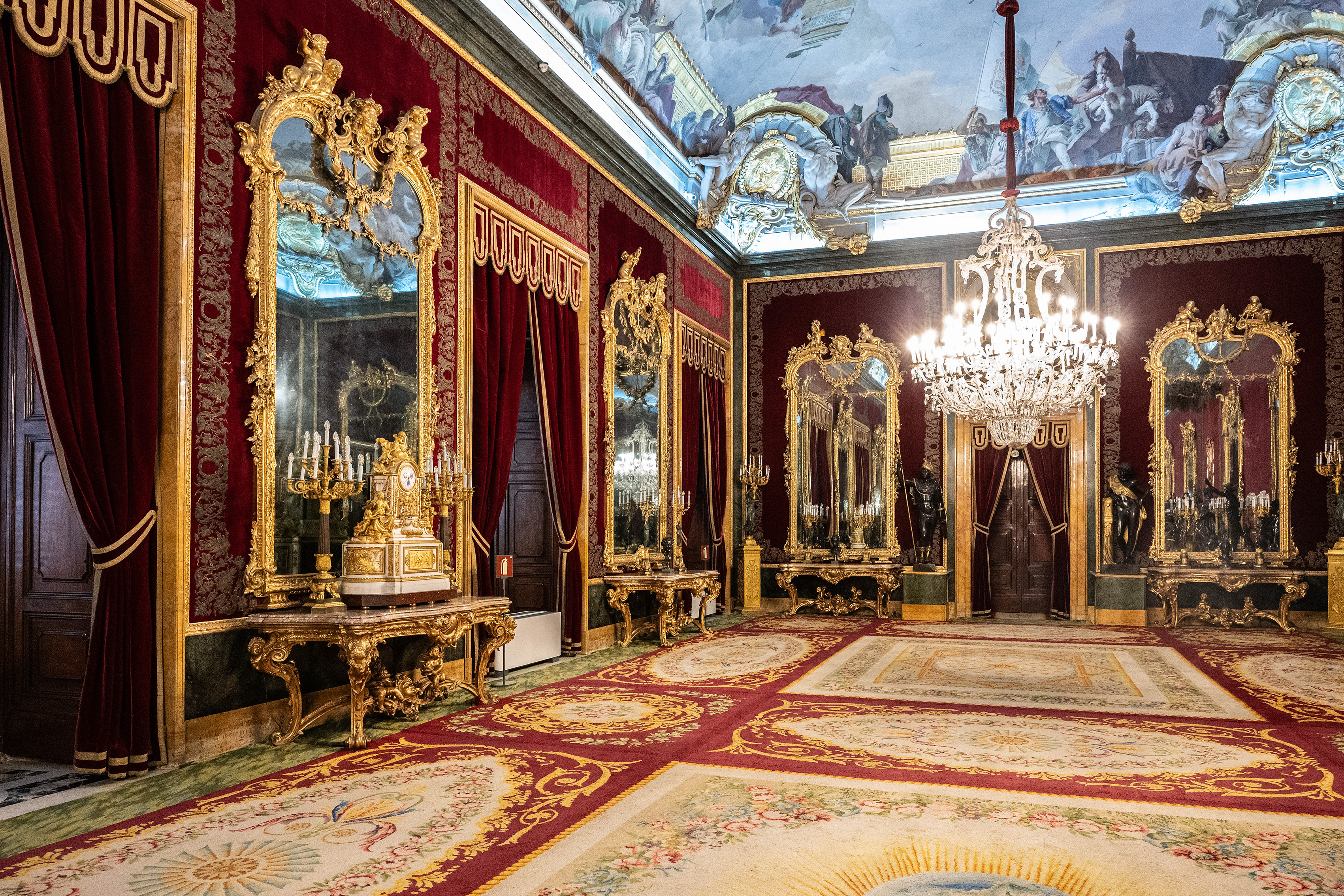 ornately decorated room with rich red walls, large gilded mirrors