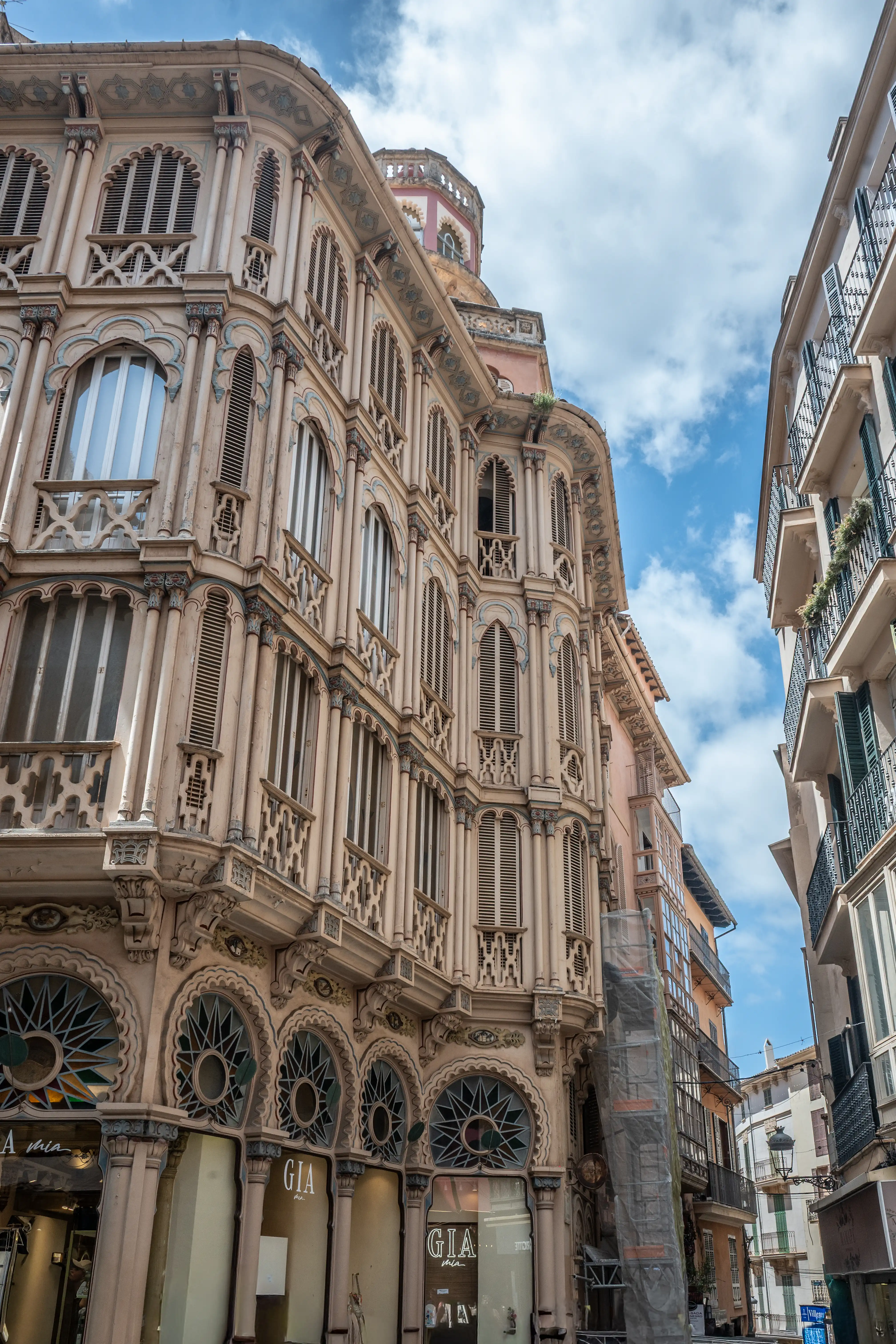 A detailed view of an ornate, multi-story building with elaborate window designs and balconies, set against a blue sky with clouds.