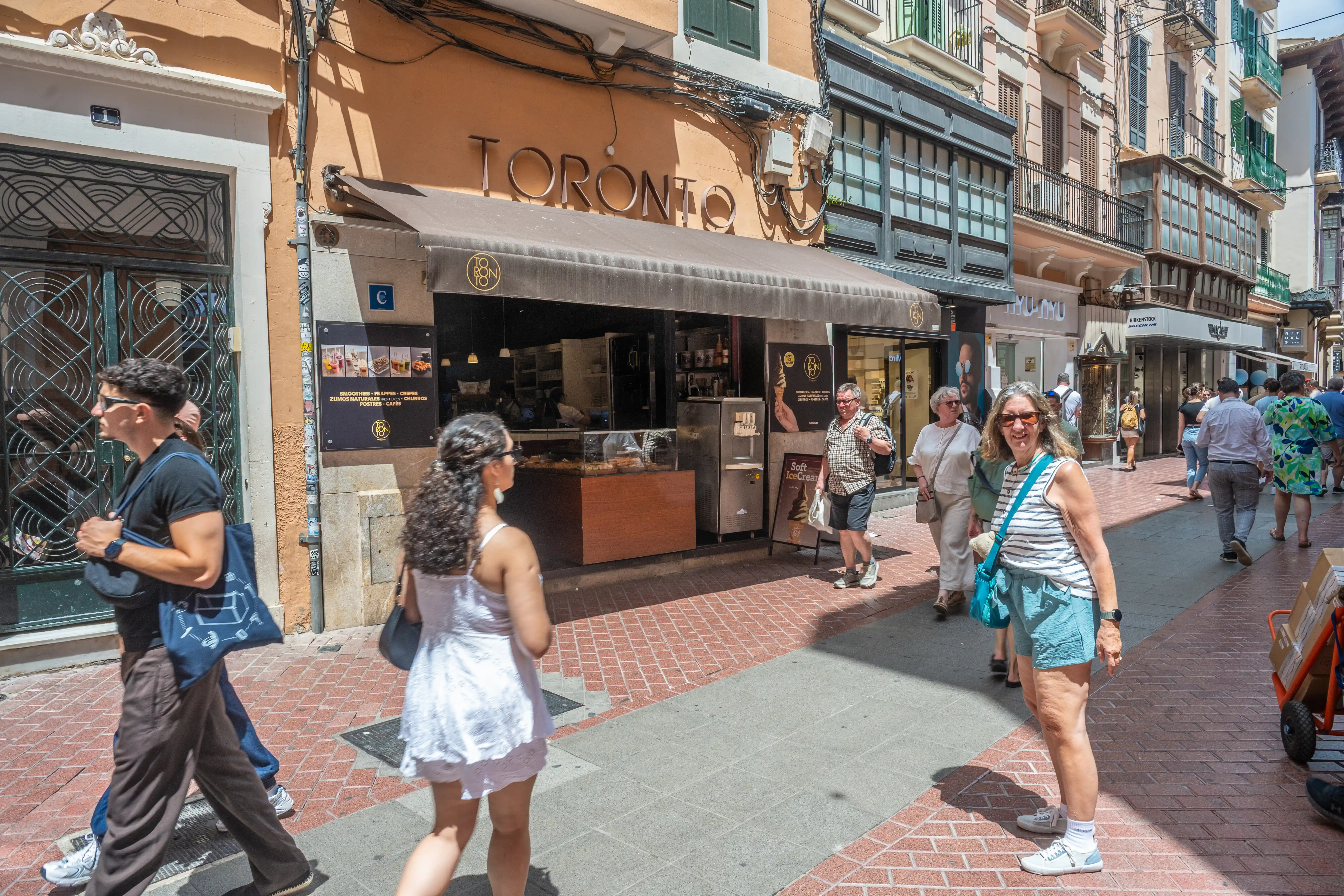 A street view of a busy pedestrian walkway lined with shops and cafes, featuring a prominent bakery named 