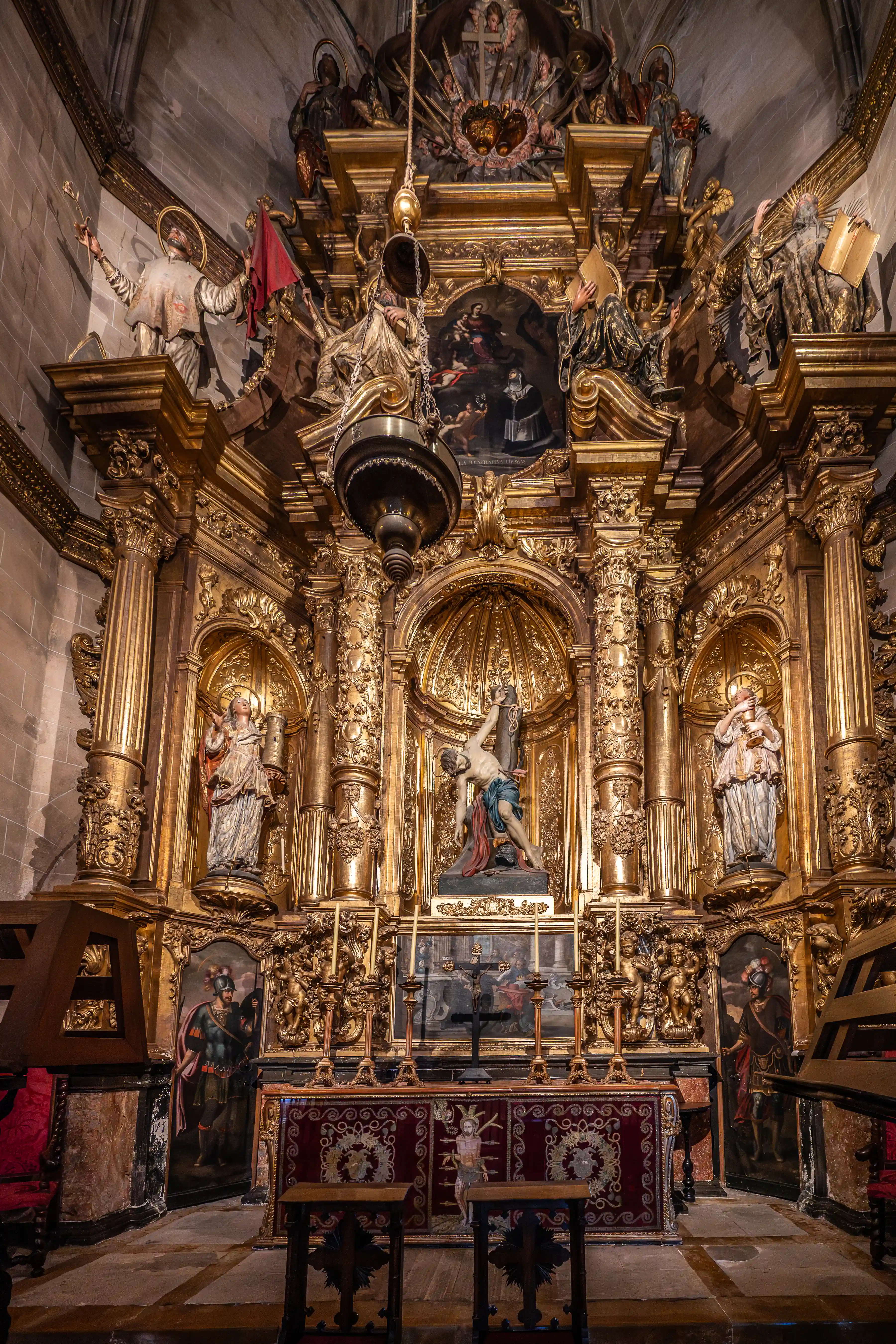 A magnificent golden altarpiece in a church, featuring a central sculpture of a crucified man, surrounded by numerous statues of saints, cherubic figures, ornate columns, and decorative panels.
