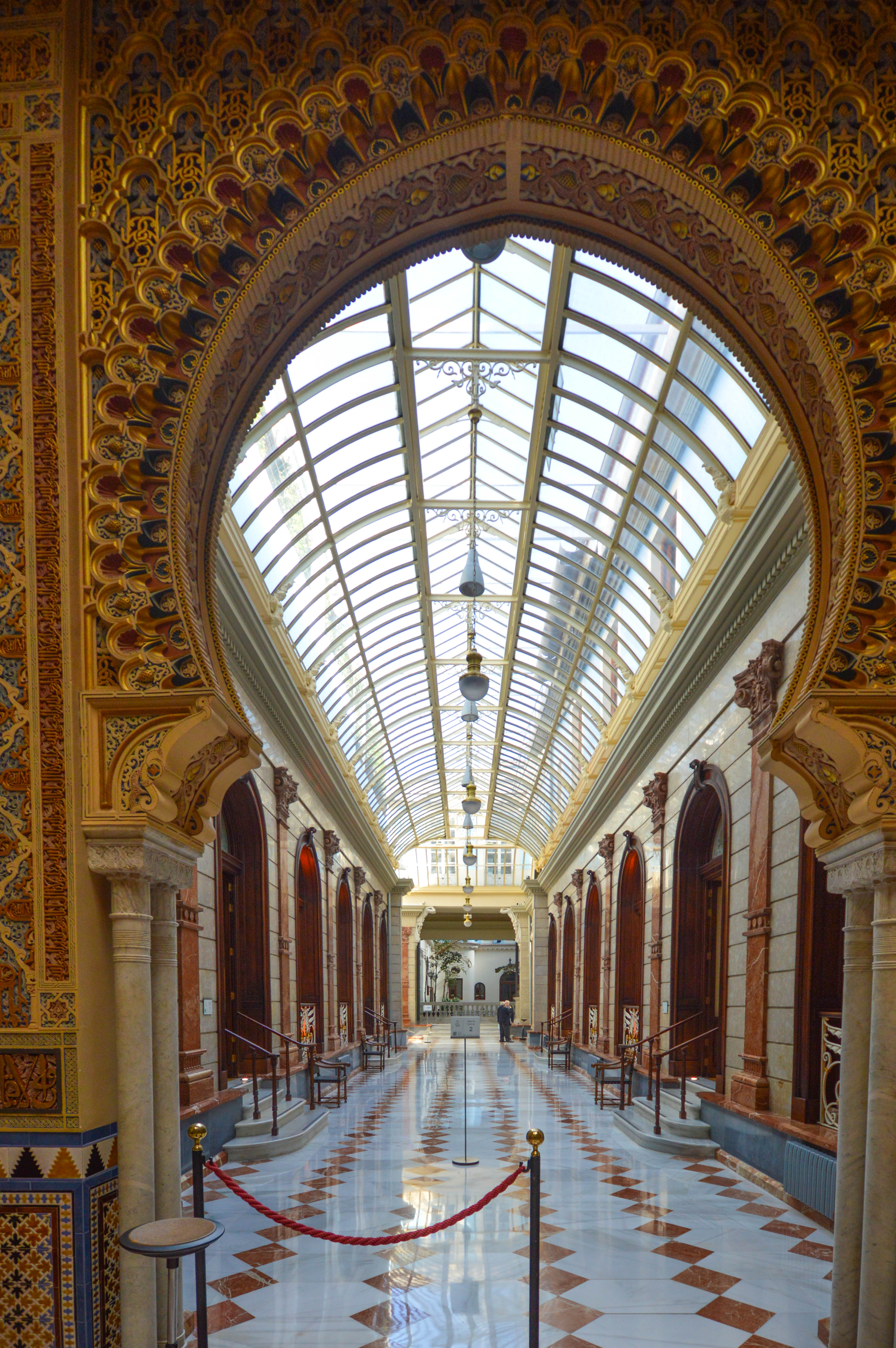 an ornate, grand hallway with a high, arched glass ceiling allowing natural light to flood the space