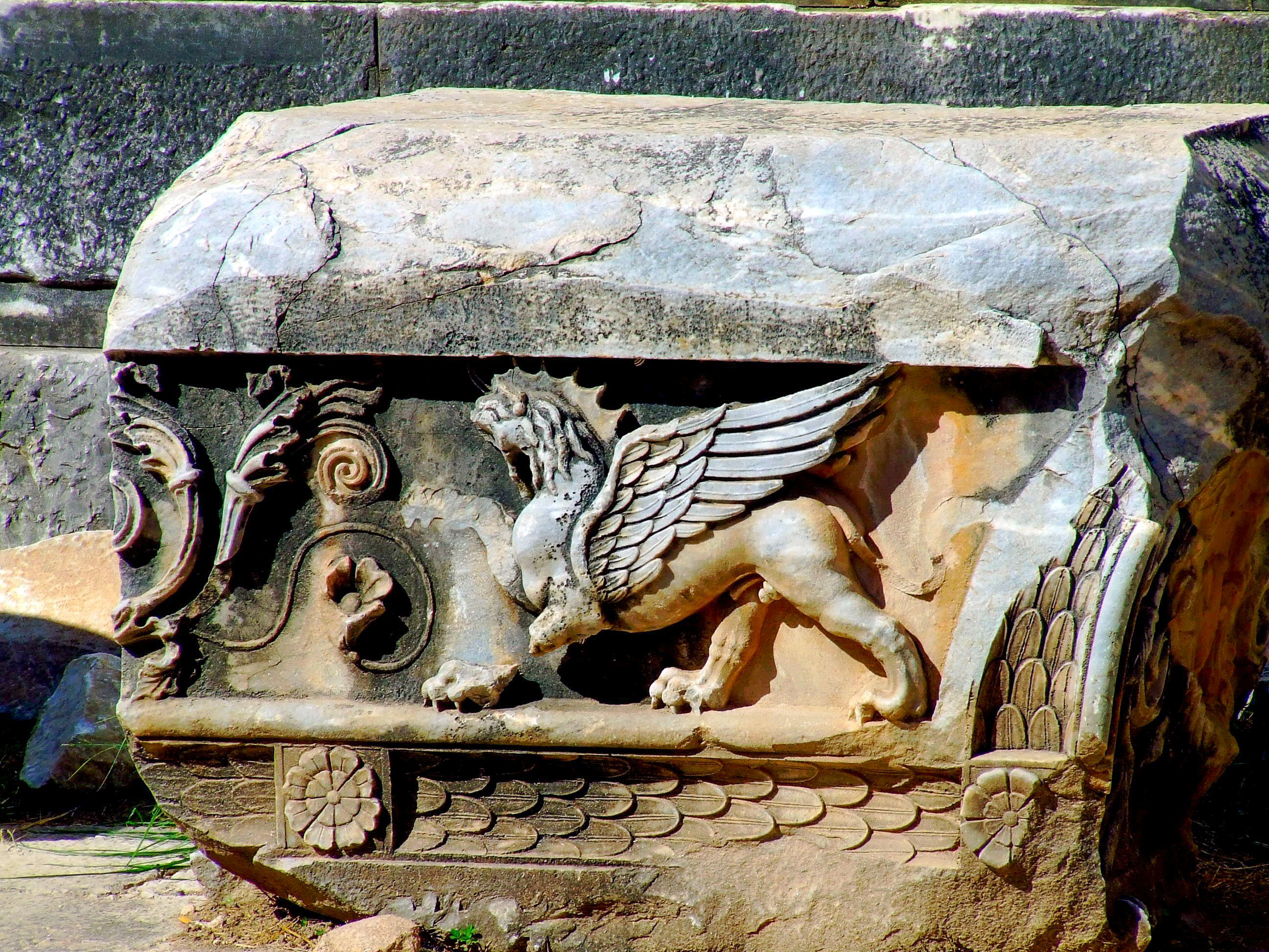 an ancient stone relief featuring a mythical creature with the body of a lion, the head of a horse, and wings, commonly known as a griffin