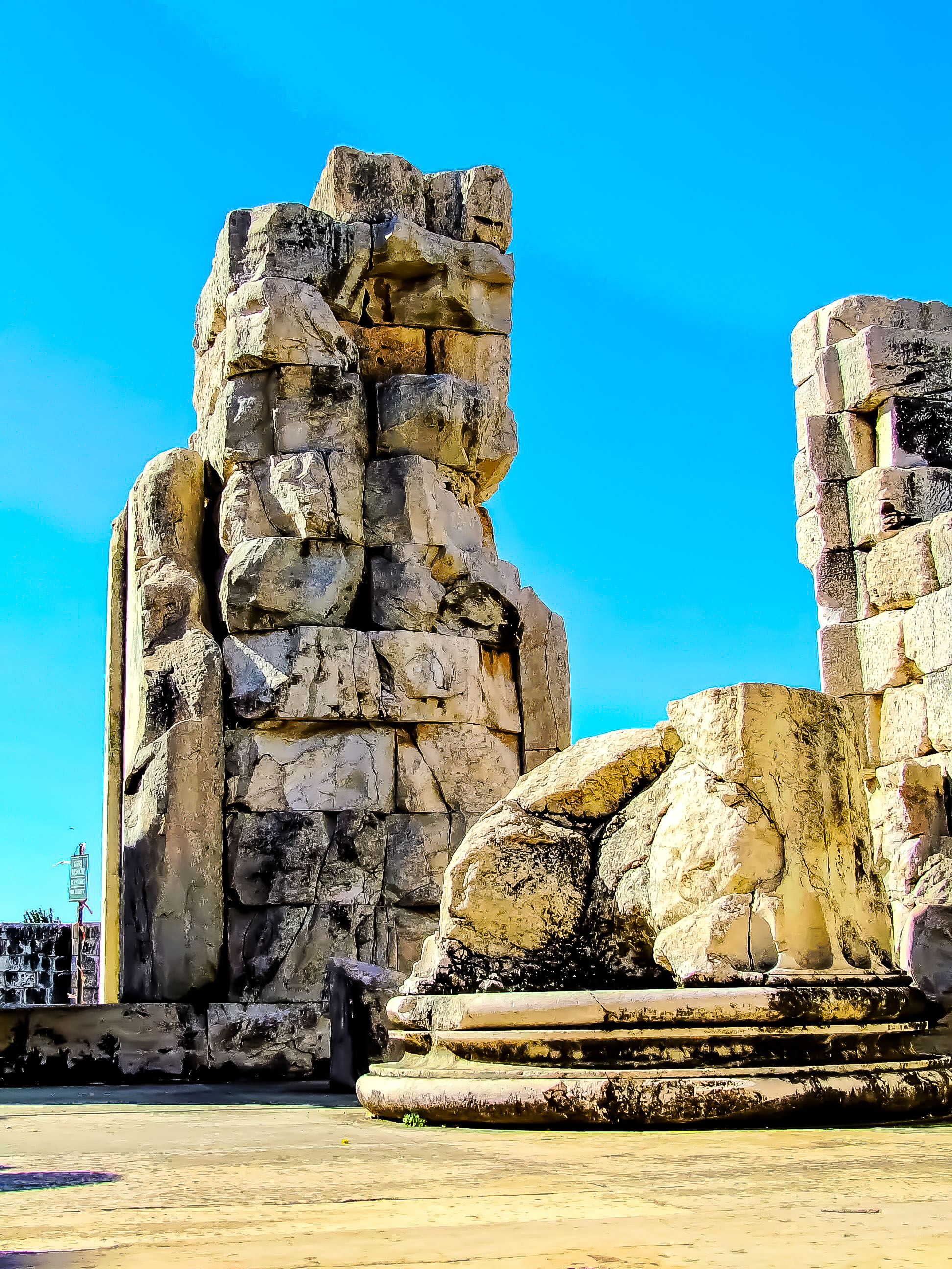 The image depicts a large, ancient stone structure, possibly a remnant of a historical monument or building. The structure appears to be made of large, roughly hewn stones stacked on top of each other, forming a tower-like shape. The stones are weathered and show signs of erosion, indicating their age. The base of the structure is wider and more solid, while the top is more irregular and jagged. The sky in the background is clear and blue, suggesting a bright, sunny day.