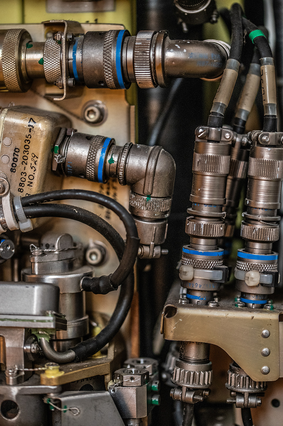 The image showcases a detailed view of a complex assembly, featuring numerous metal connectors and black cables. Several connectors have blue bands and some are labeled with numbers. The arrangement suggests a sophisticated electronic or mechanical system, possibly from an aircraft or industrial equipment, characterized by its robust and interconnected nature.
