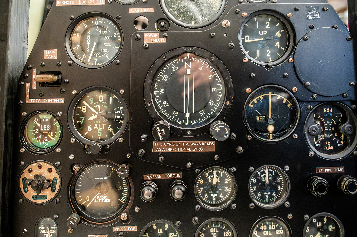 The image shows a detailed view of an aircraft's instrument panel, featuring various gauges and dials that provide critical flight information such as airspeed, altitude, fuel levels, and directional guidance. The instruments include a directional gyro, altimeter, airspeed indicator, fuel gauges, and engine temperature indicators. Labels and markings on the instruments offer specific data points and operational instructions necessary for pilot navigation and aircraft management. The panel appears to be from an older aircraft, given the style and design of the instruments. Overall, the image captures the complexity and importance of the instruments used in aviation for safe and effective flight operations.