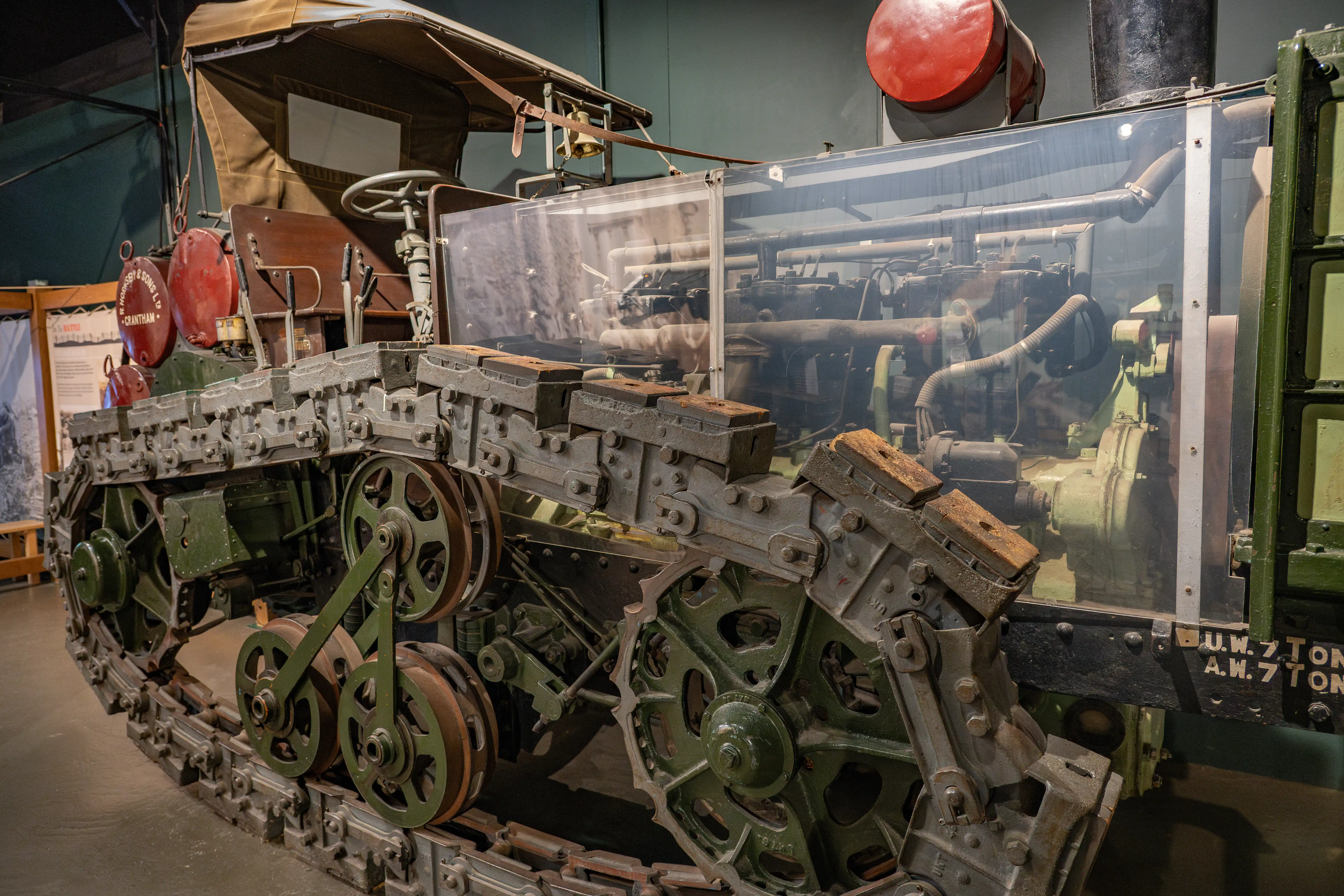 The image depicts an old, possibly antique, machine with a complex mechanical structure. The machine is encased in a protective cover, likely for display purposes. The visible components include large gears, belts, and various metallic parts, indicating it might be an industrial or agricultural machine from a bygone era. The machine has a greenish hue, suggesting it has been exposed to the elements or has been preserved in that state. There are also red spherical objects attached to the machine, which could be part of the machinery or safety features.