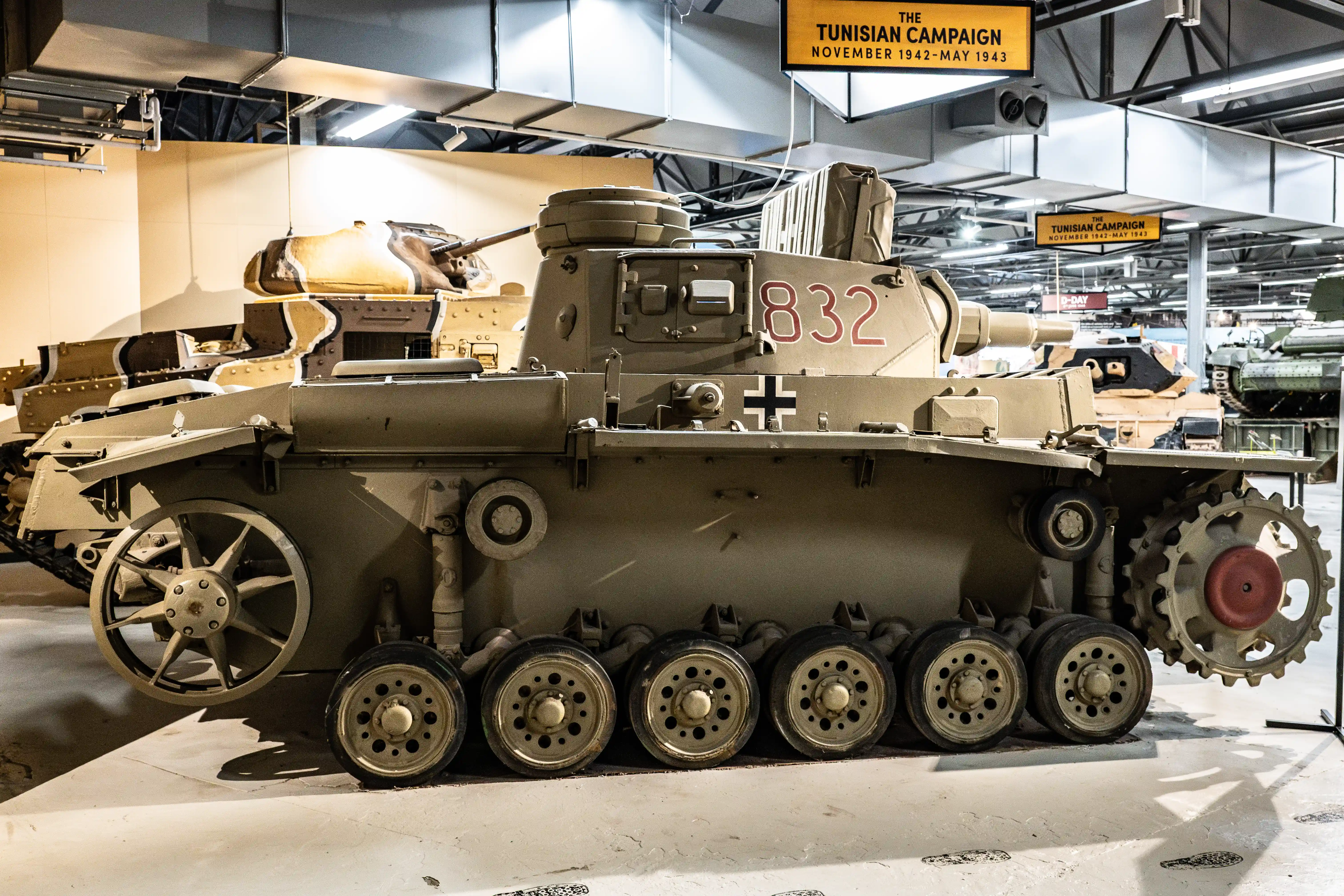 The image shows a tank, specifically a Panzerkampfwagen II, on display in a museum. The tank is marked with the number 832 and a cross insignia. It is part of an exhibit related to the Tunisian Campaign, which took place from November 1942 to May 1943, as indicated by the signage above the tank.