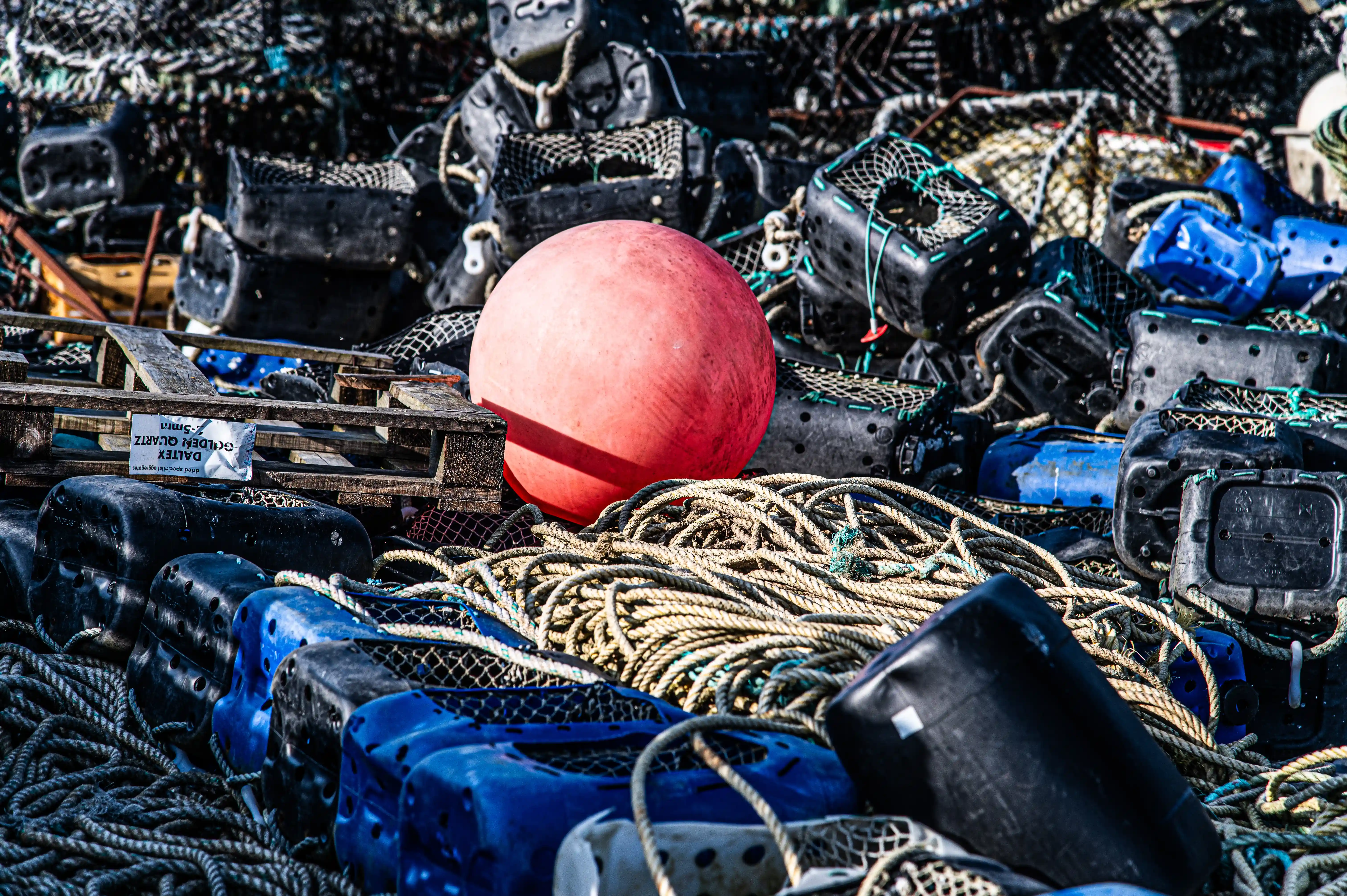Talk about a busy fishing spot! This close-up shot shows a jumbled collection of what looks like fishing equipment. There's a large, bright red ball (possibly a buoy), lots of rope coiled up, and various black and blue plastic containers and nets. It gives you a sense of the tools of the trade for someone who works on the water.