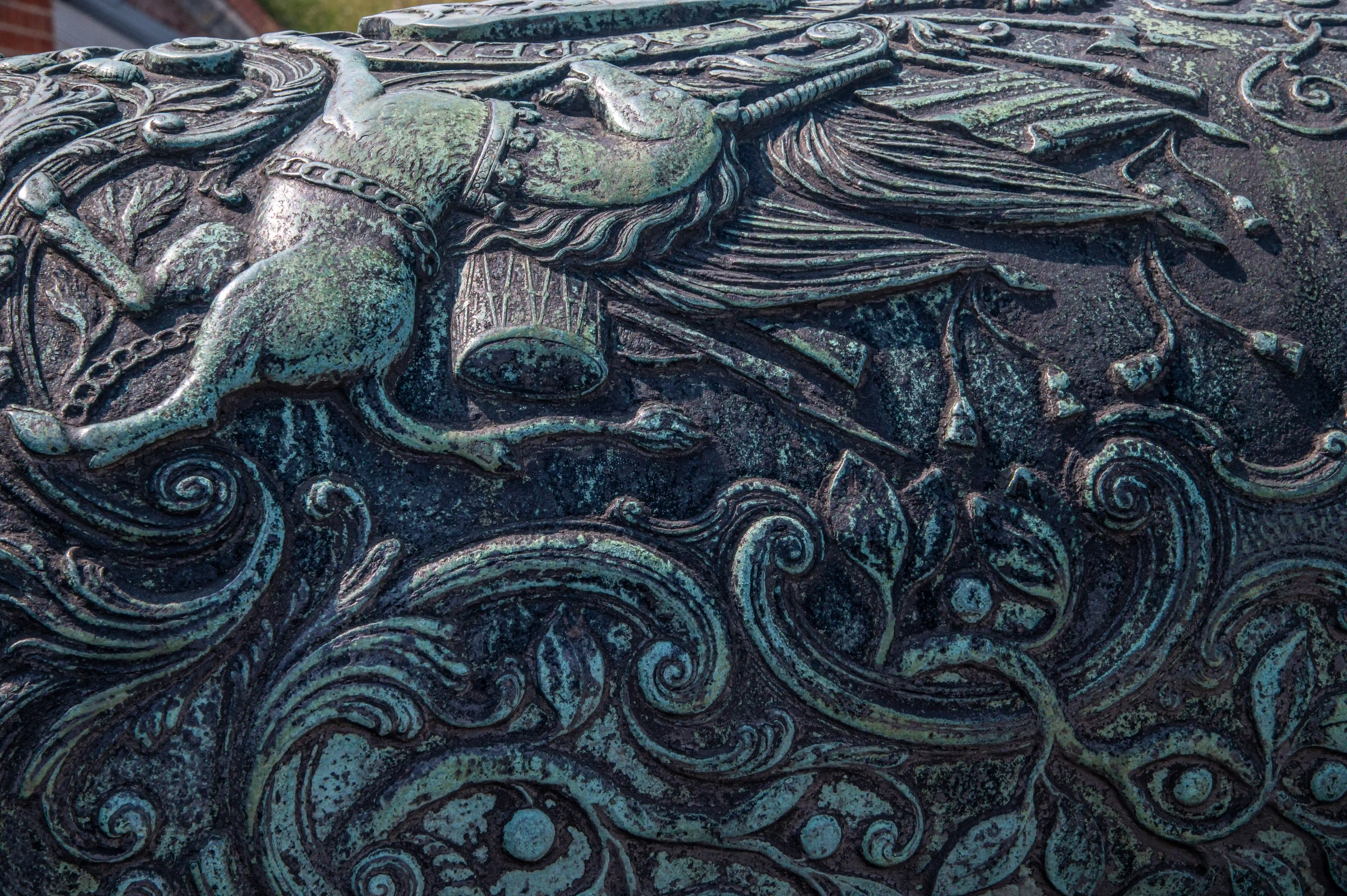 The image depicts an intricate sculpture featuring a detailed, stylized fish or aquatic creature with flowing, wavy patterns surrounding it. The sculpture appears to be made of a dark, weathered metal, possibly bronze, and exhibits a high level of craftsmanship with elaborate detailing.