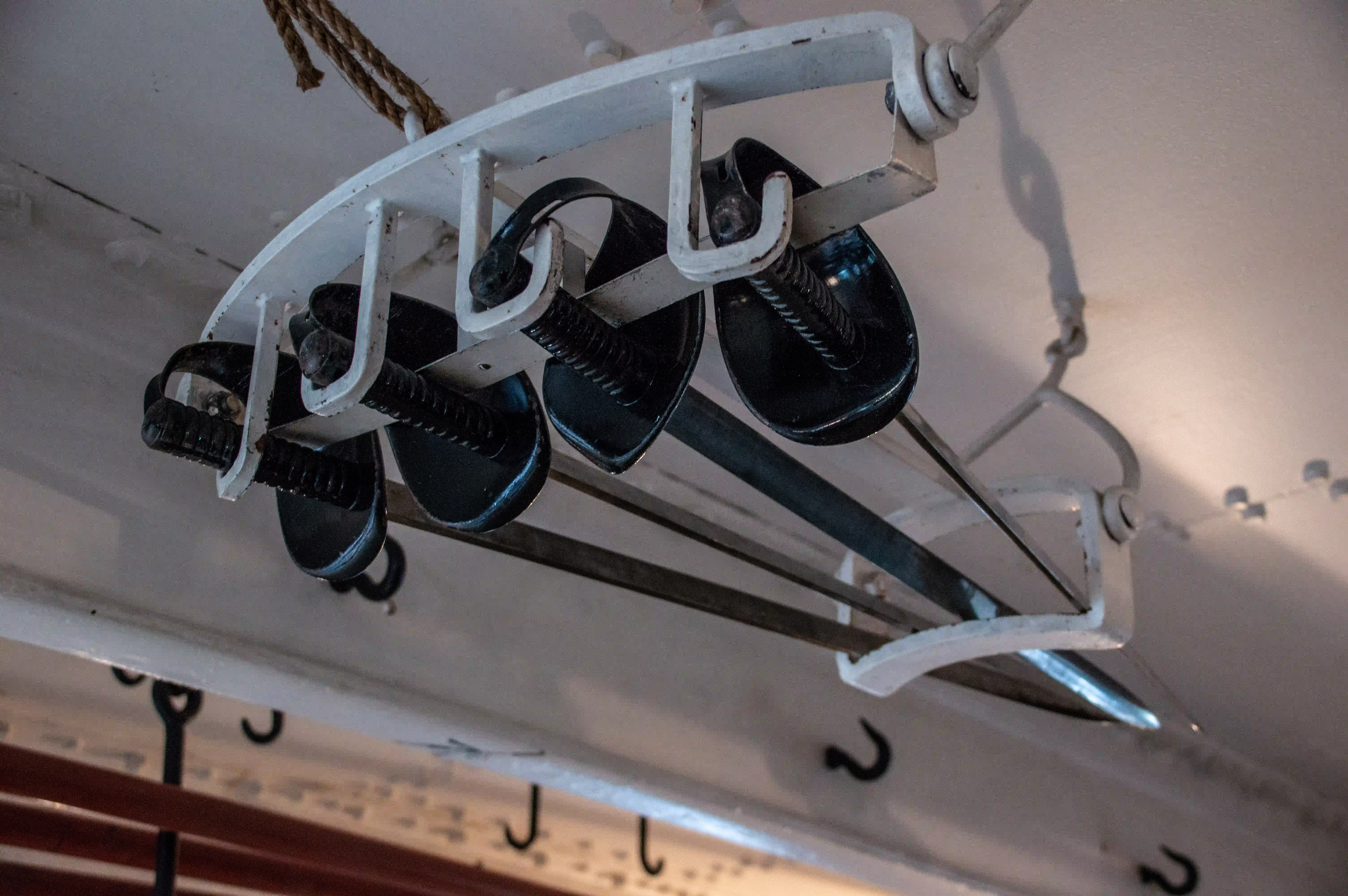 The image shows a close-up of a pulley system with multiple sheaves, likely used for lifting or moving heavy loads. The pulleys are mounted on a white metal frame, and the system is secured with bolts and screws. The background appears to be part of a ship or a similar structure, indicated by the visible wooden planks and metal hooks.