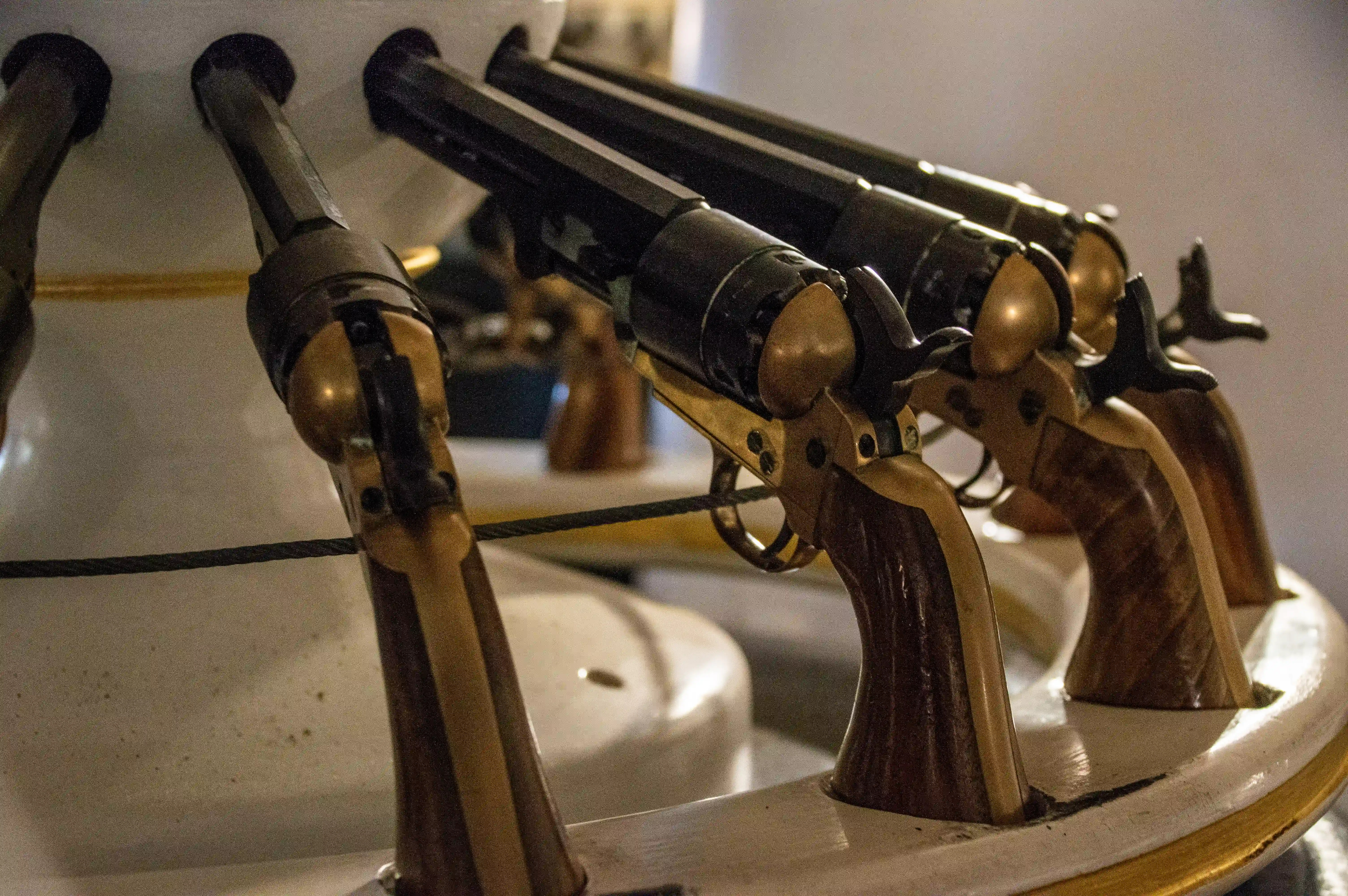 The image shows a close-up view of an antique sewing machine, highlighting its intricate metal components and mechanisms. The machine features a series of metal arms and knobs, likely used for various sewing functions. The overall design suggests it is an older model, possibly from the late 19th or early 20th century. The metal parts have a worn, aged appearance, indicating they have been well-used over time. The background is blurred, focusing attention on the detailed craftsmanship of the sewing machine.