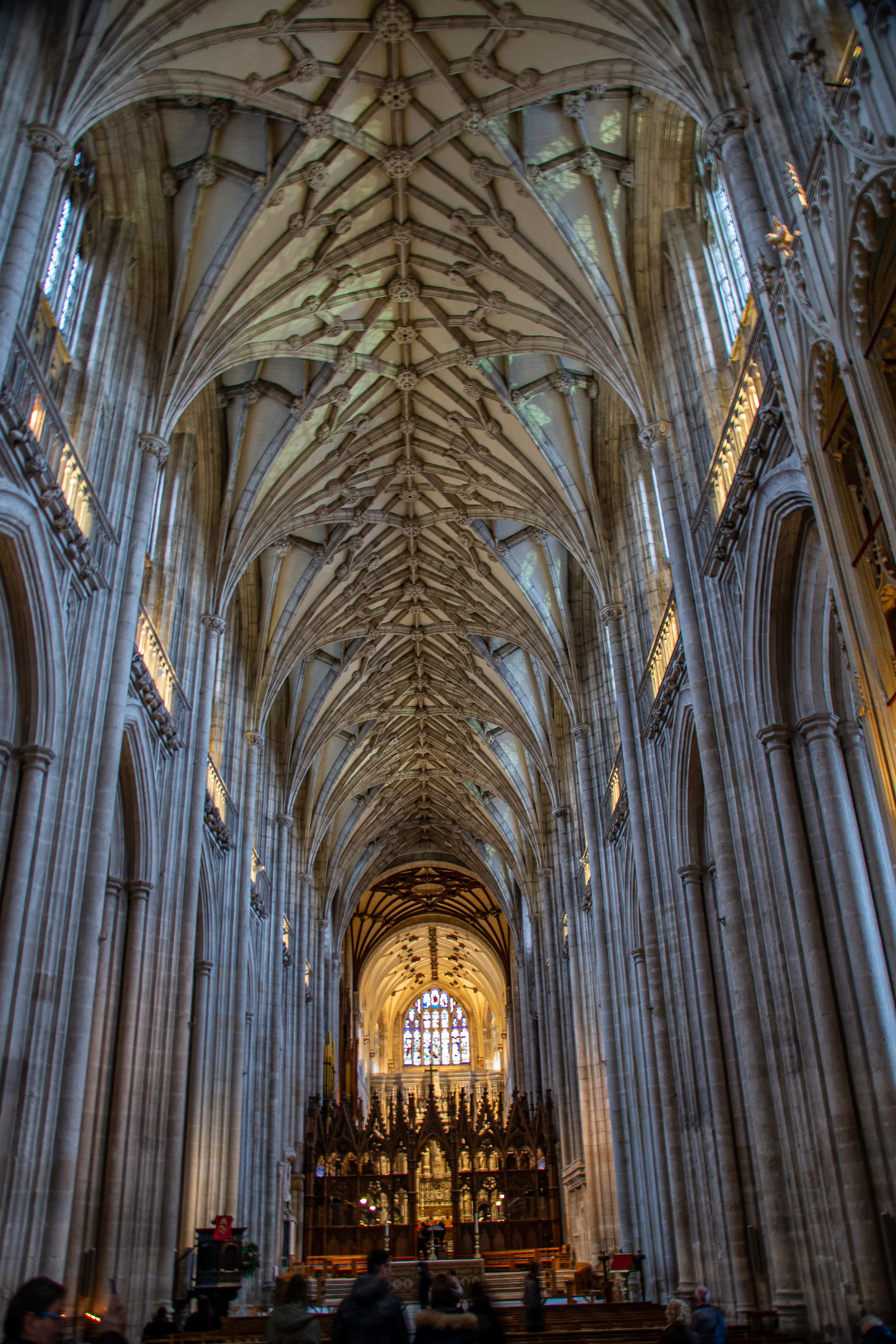 The image depicts the interior of a grand cathedral, showcasing its impressive Gothic architecture. The ceiling features intricate vaulting with ribbed arches, and the space is illuminated by natural light filtering through stained glass windows. Tall, slender columns line the nave, leading the eye towards the ornate altar at the far end. The detailed craftsmanship and the sheer scale of the structure highlight the architectural prowess and artistic sensibilities of the era in which it was built.