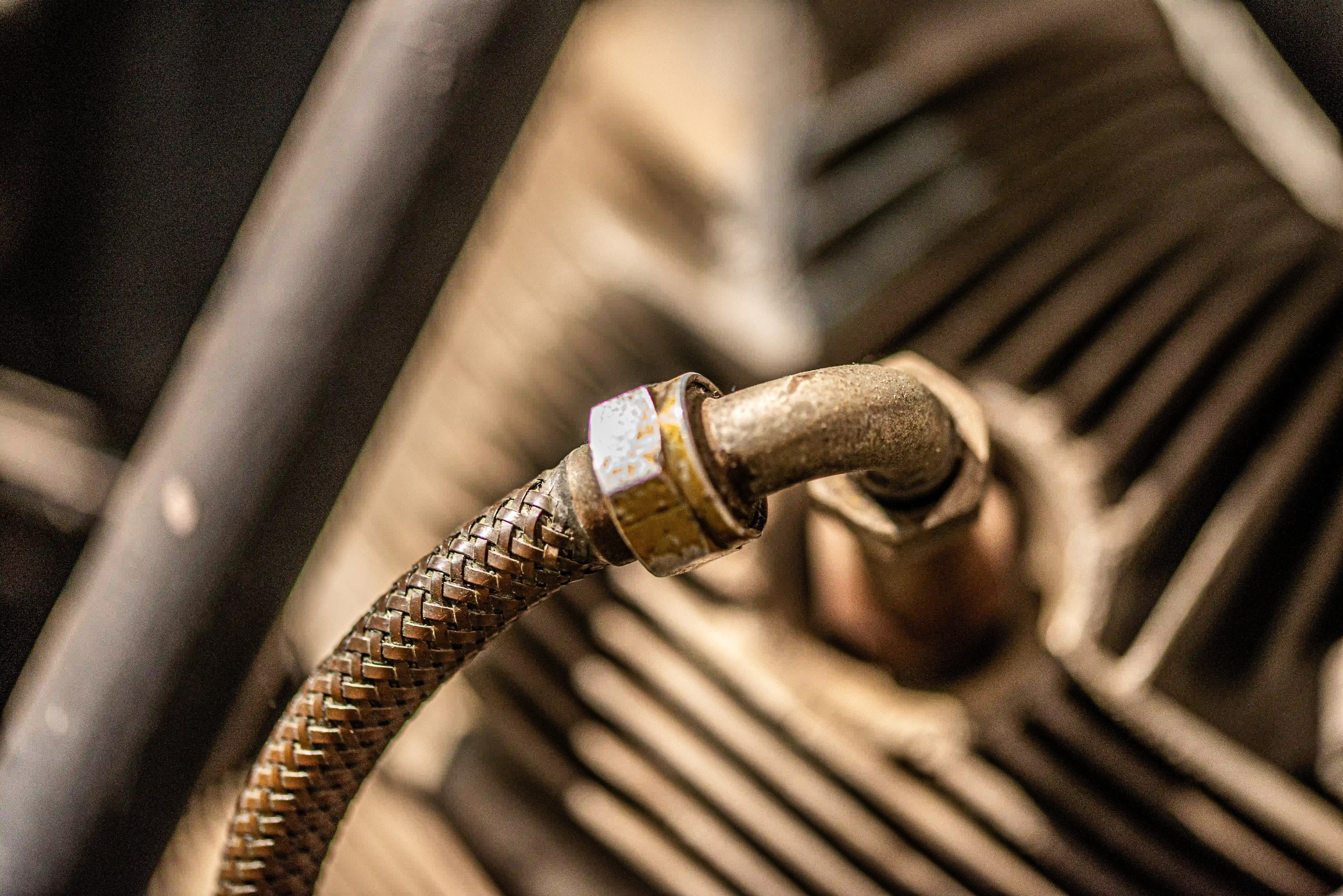 Close-up of a metal braided hose connected to a metal pipe fitting on a textured, finned surface.