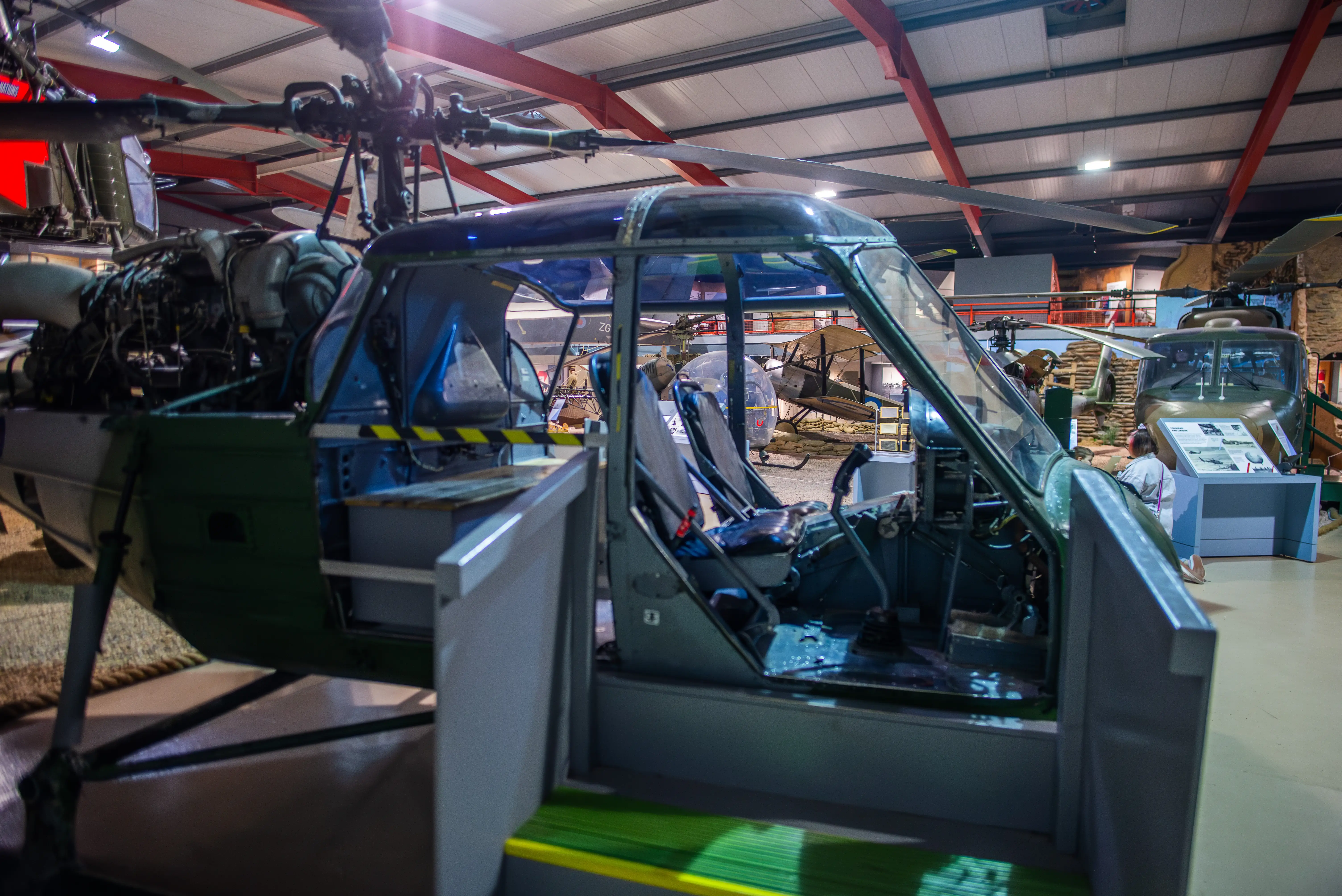 Close-up museum display of a military helicopter cockpit and engine section with surrounding aircraft exhibits.