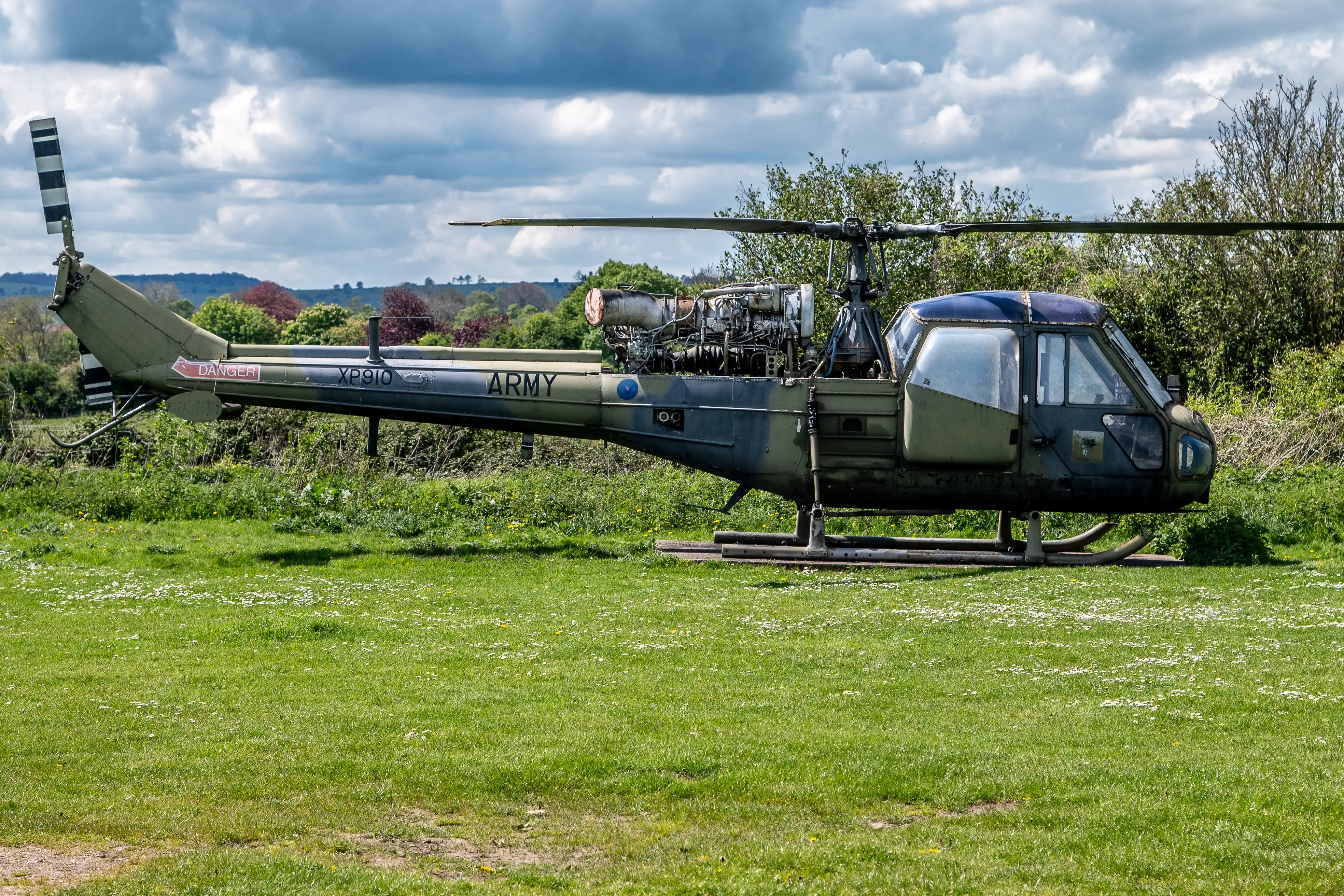 Olive-green British Army helicopter on a grassy field with open engine compartment and tail code XP910.