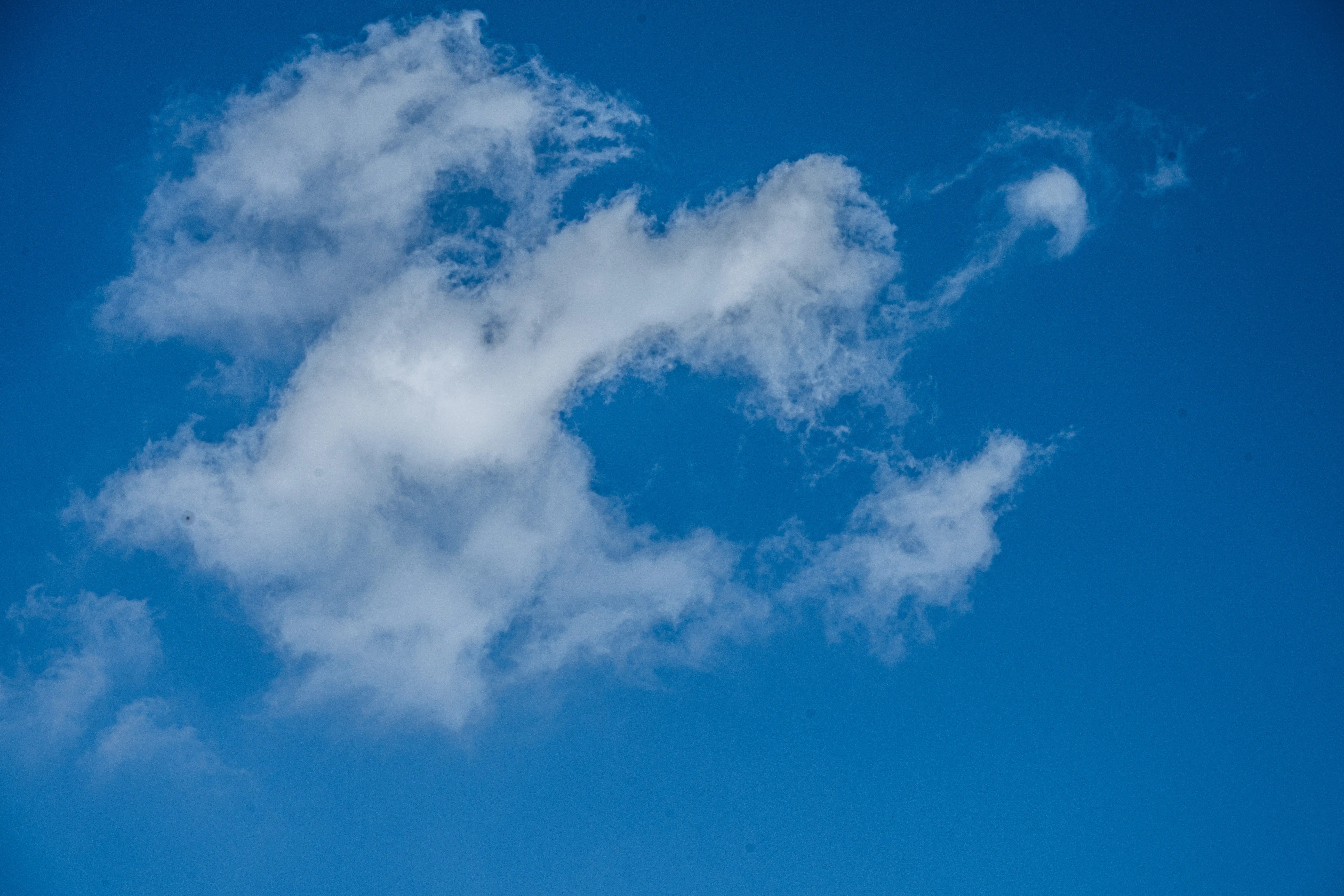 The image depicts a clear blue sky with a few scattered, wispy white clouds. The clouds are sparse and appear to be thin, suggesting a fair weather day. The sky is predominantly a deep blue, indicating a lack of significant atmospheric interference. The overall scene conveys a sense of calm and tranquility.