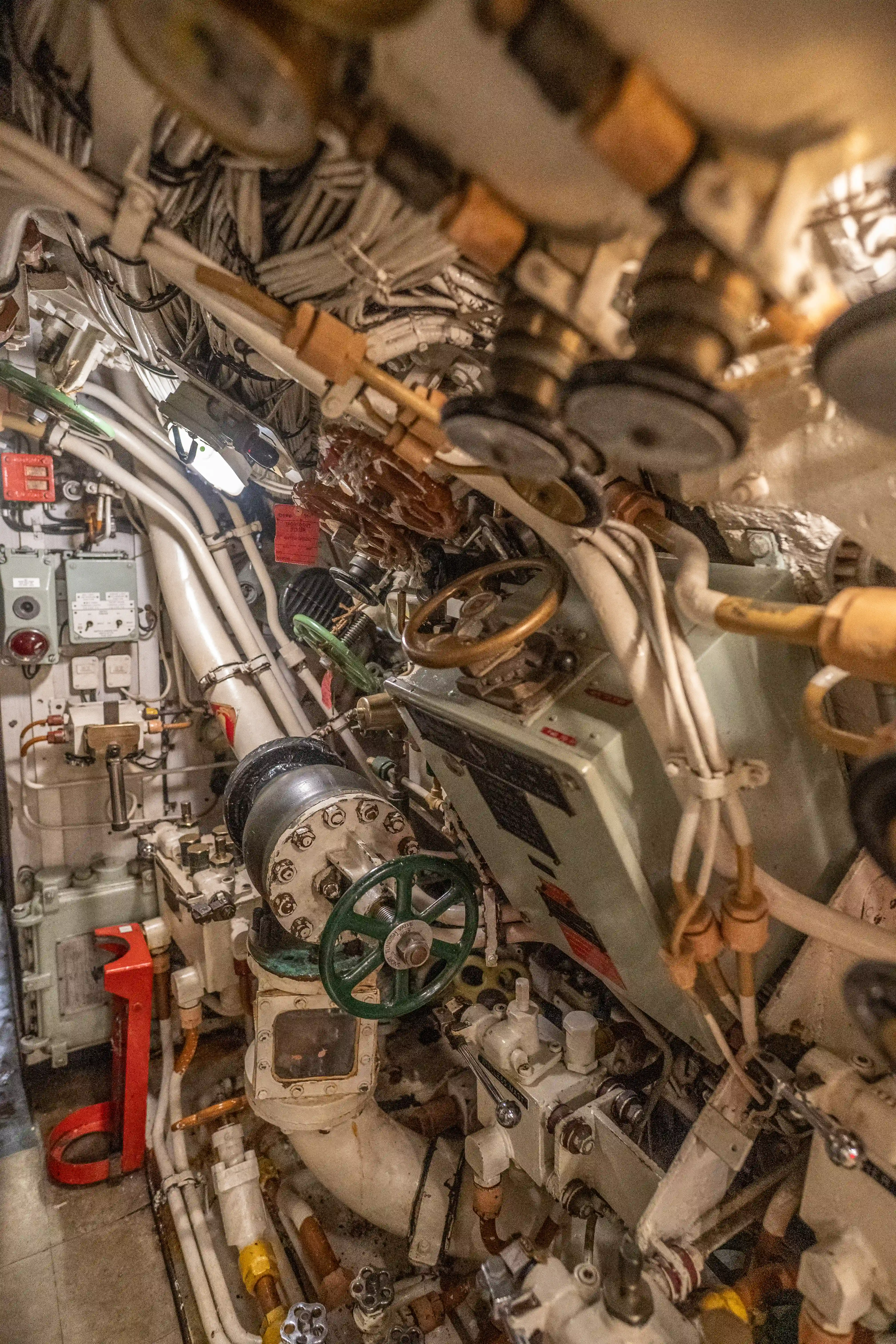 The image depicts a complex and densely packed mechanical room, likely the control or engine room of a submarine or ship. Various pipes, valves, gauges, and control mechanisms are visible, indicating a highly functional and intricate system. The equipment appears well-used, with some signs of wear and tear. The space is confined, showcasing the compact nature of such environments. The overall scene highlights the technical complexity and operational intricacies involved in managing such machinery.