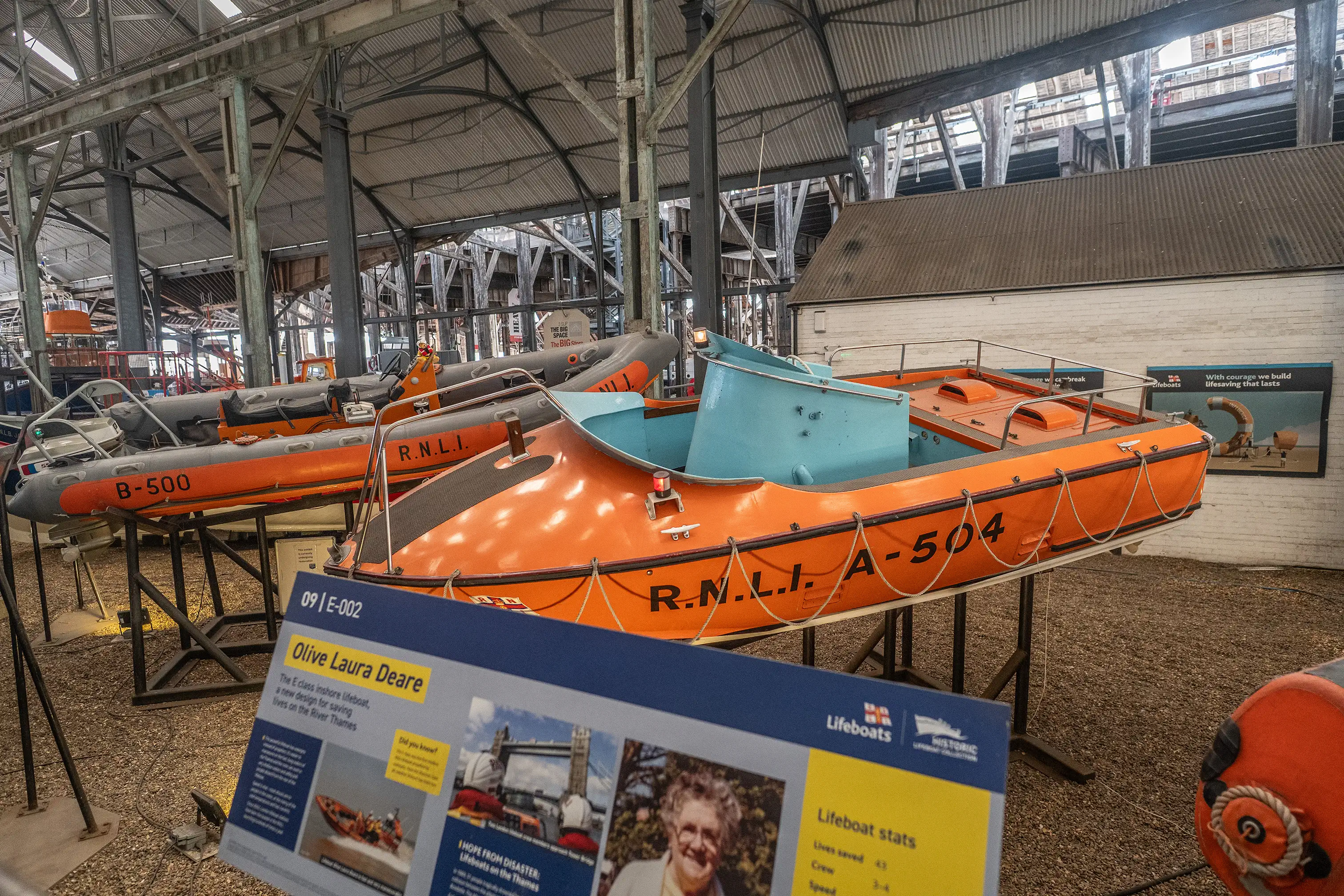 A display of RNLI lifeboats, with a prominent orange lifeboat 'A-504' in the foreground and an information plaque for the 'Olive Laura Deare'.