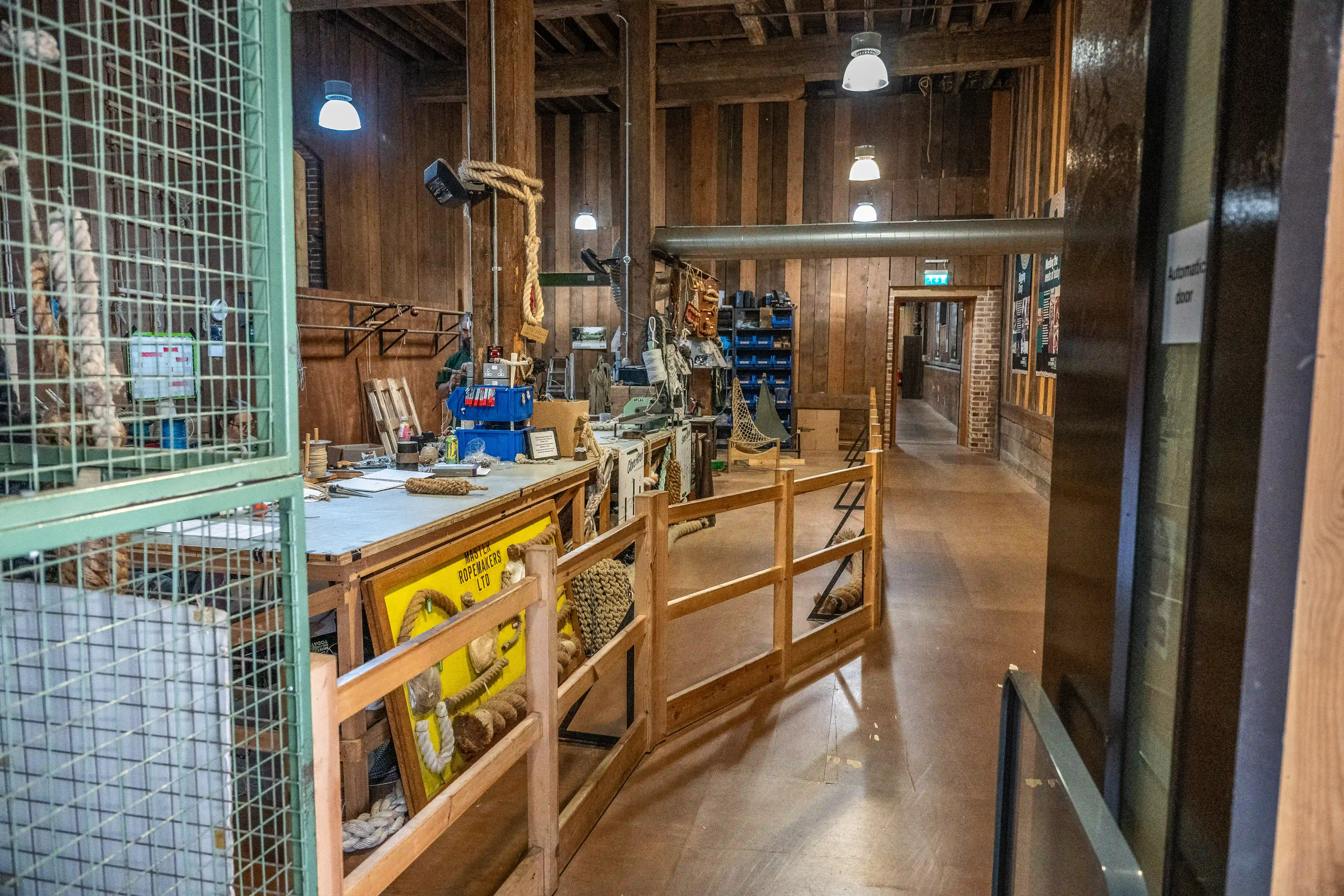  Interior of a rope making workshop with wooden walls, rope displays, tools, and a cage.