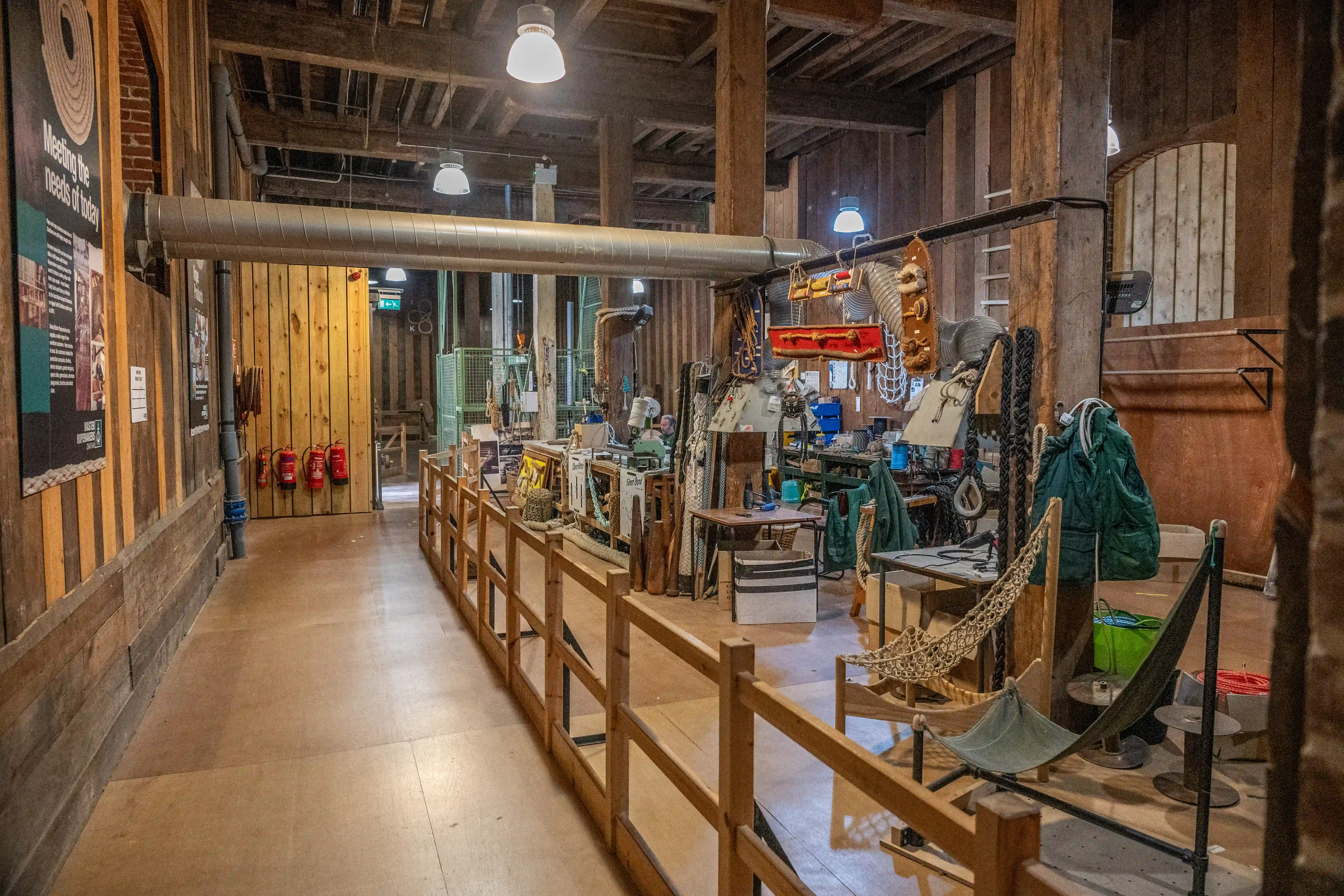 Interior view of a historical industrial workshop with wooden structures, display cases, tools, ropes, and a suspended duct.