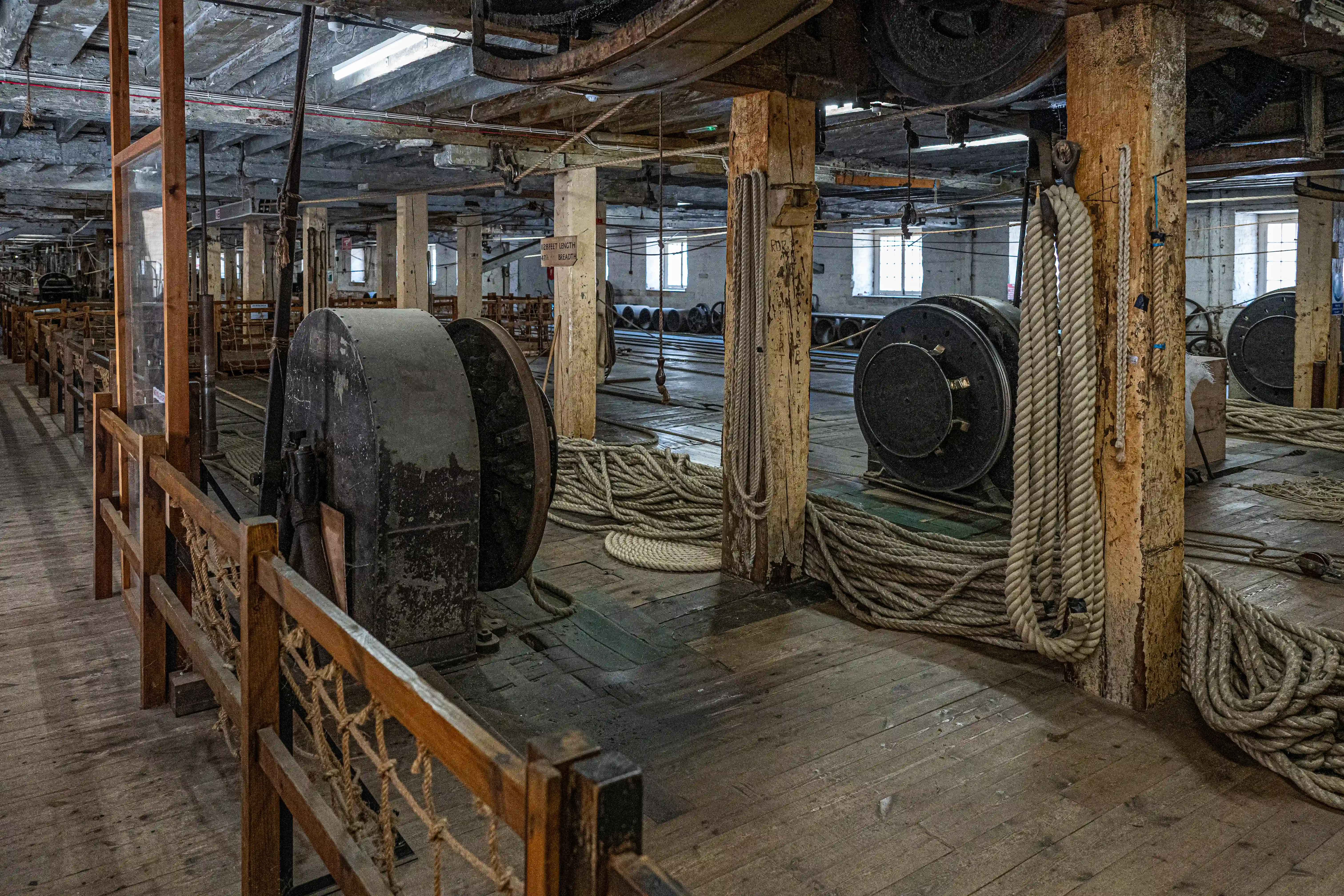 Interior of a disused rope factory with large spools of rope, wooden floor, and exposed industrial machinery.