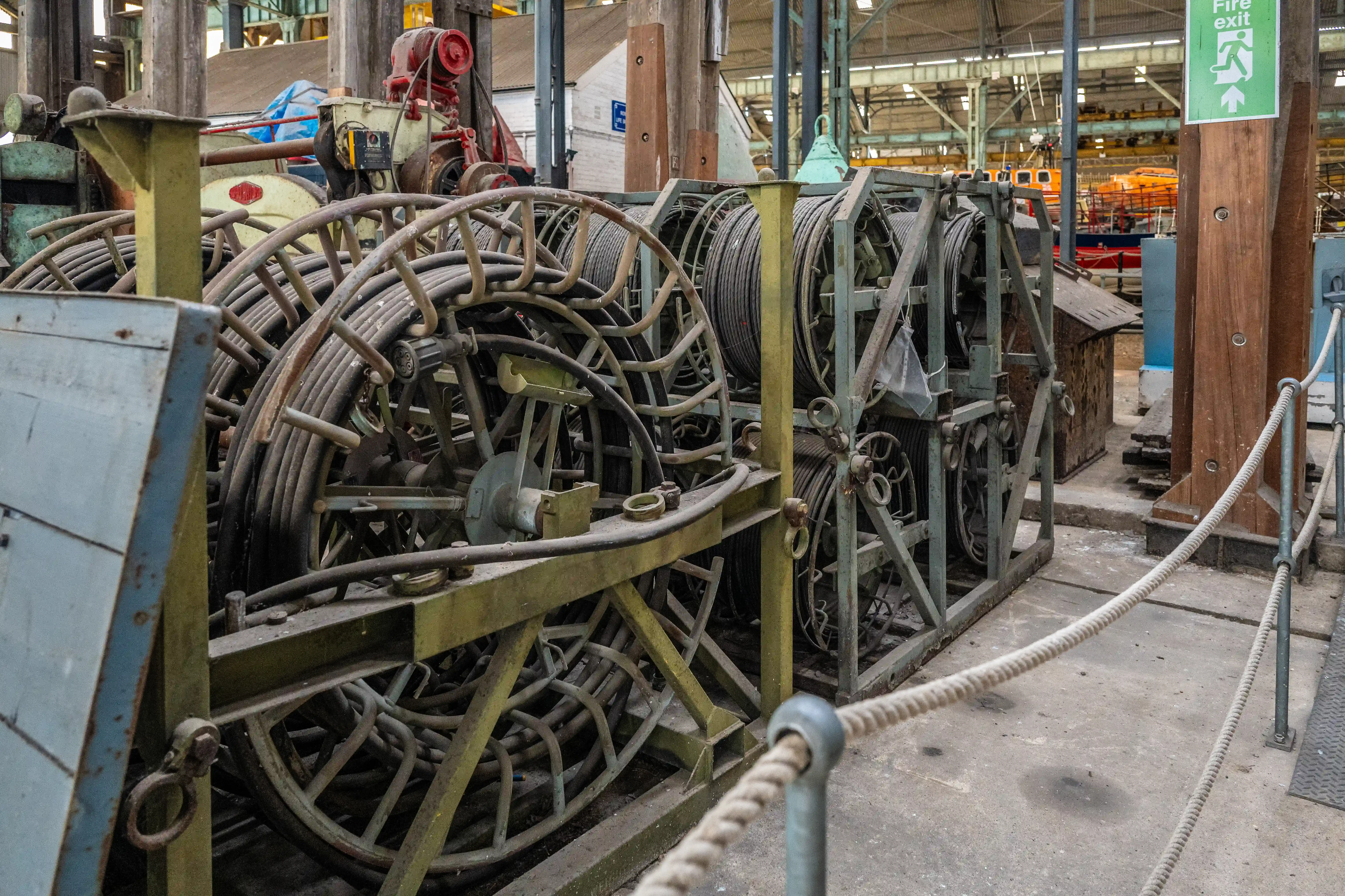Industrial cable reels and machinery in a workshop, with a fire exit sign in the background.