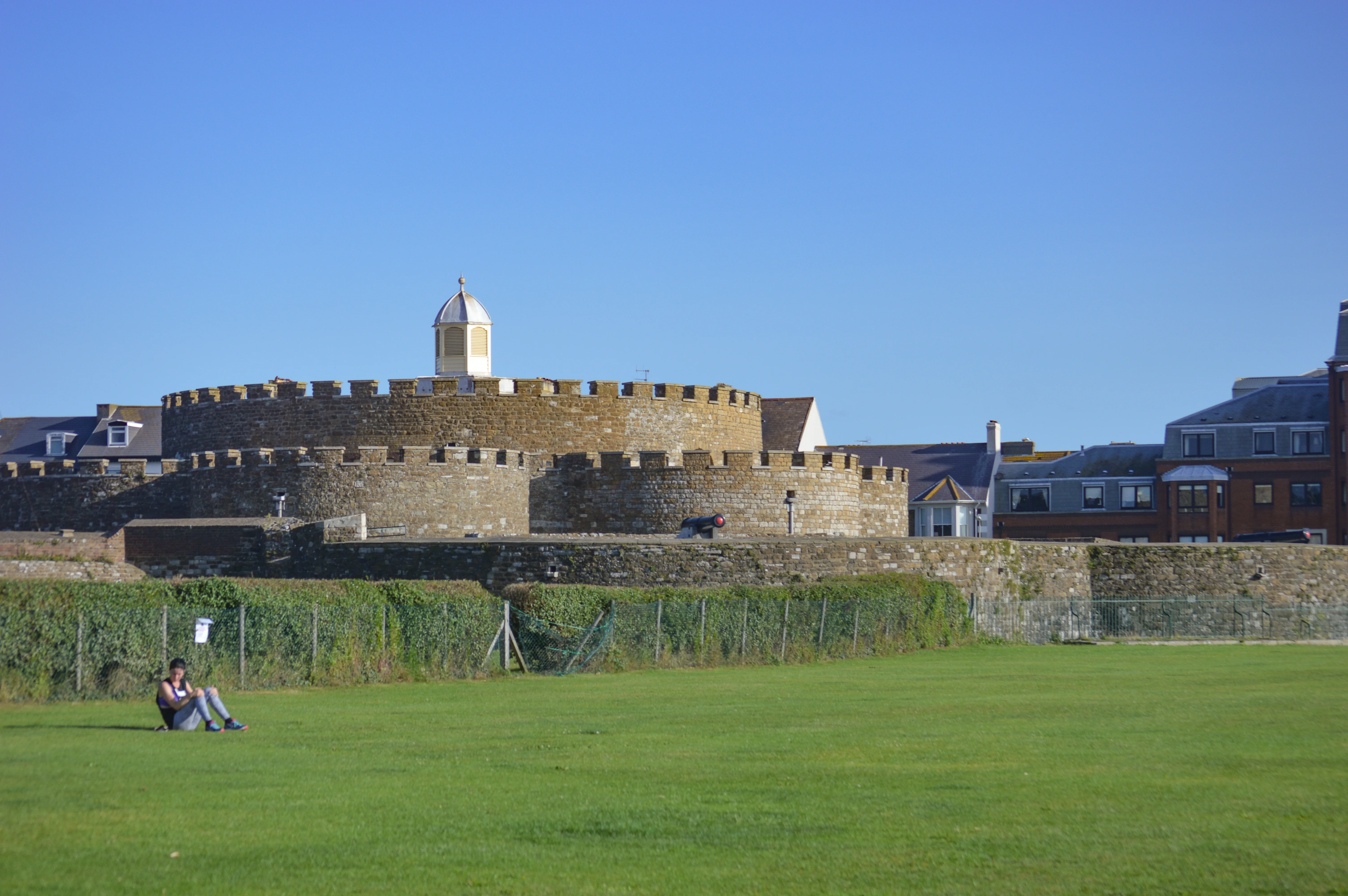 A stone fort with battlements and a dome, with a person sitting on a green lawn in the foreground.