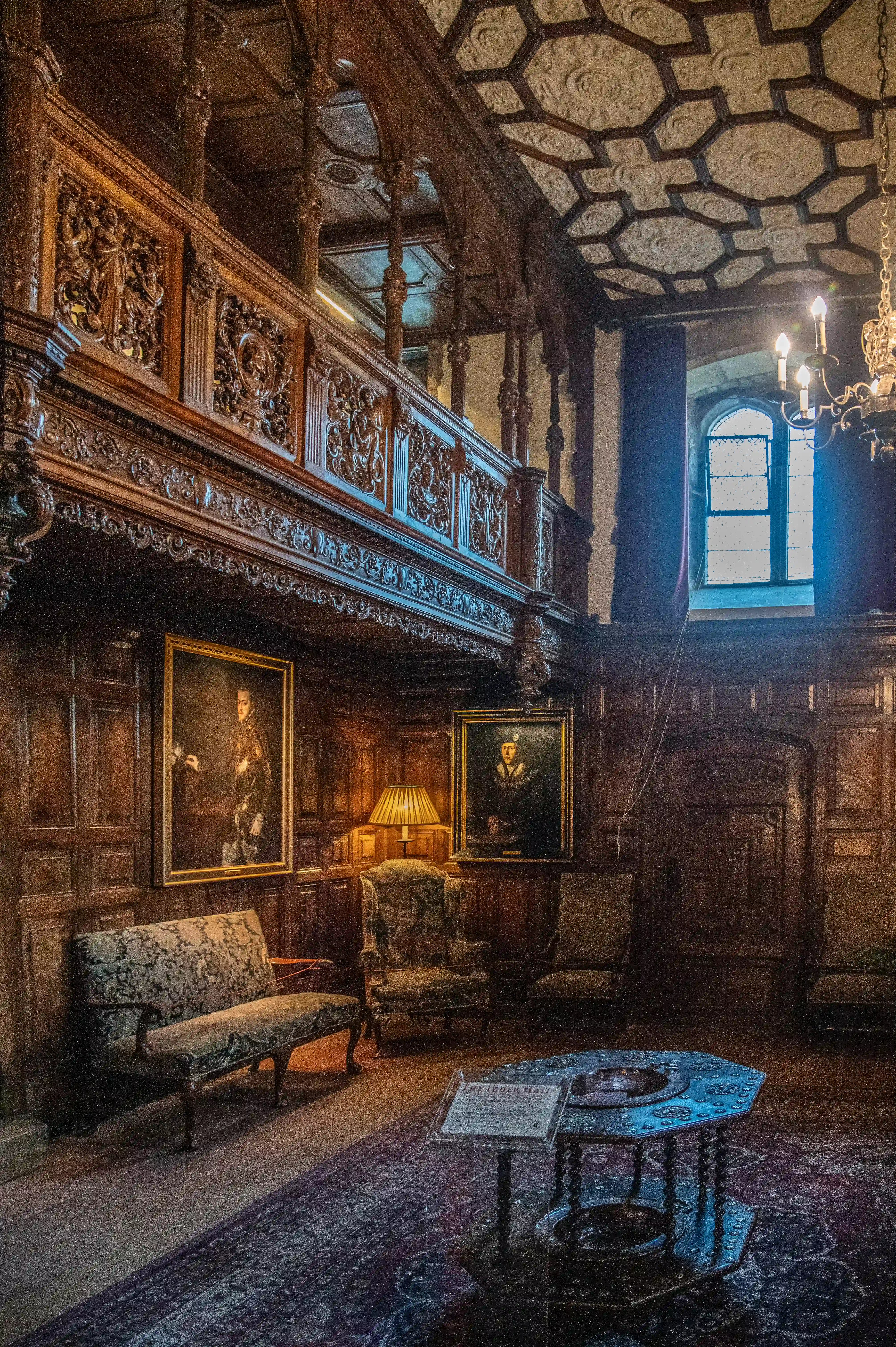 Interior of a grand historic room with dark wood panelling, a carved balcony, formal portraits, antique seating, and a coffered ceiling.