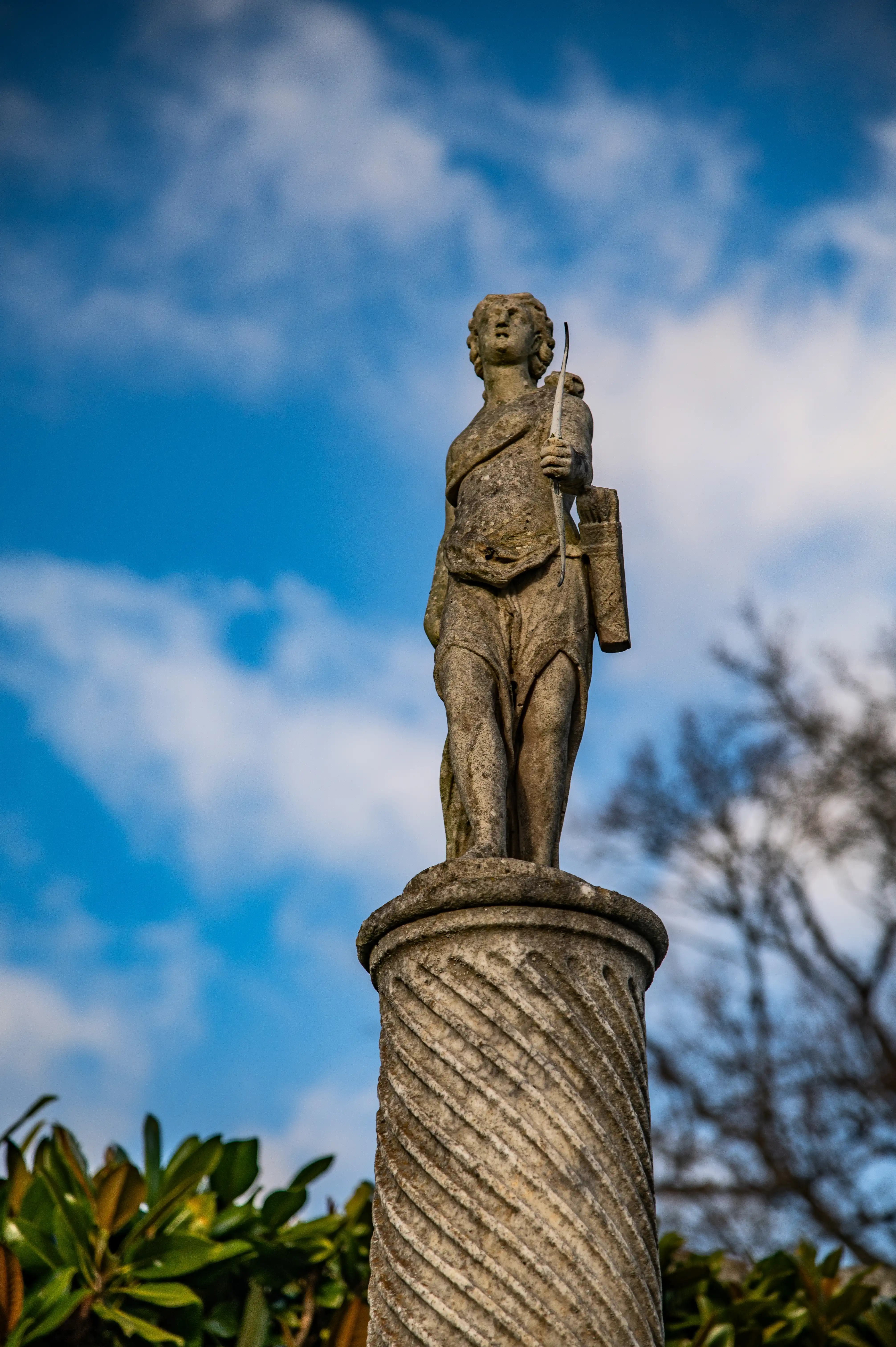 A stone statue of an archer on a carved pedestal against a blue sky with clouds.