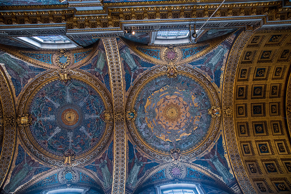 The image showcases an intricately designed ceiling with two large, ornate circular patterns. Each circle features detailed artwork with a mix of blue, gold, and other colors, surrounded by elaborate borders. The ceiling also includes smaller decorative elements and structural supports. The overall design is rich and elaborate, suggesting a historical or culturally significant building, such as a cathedral or palace.