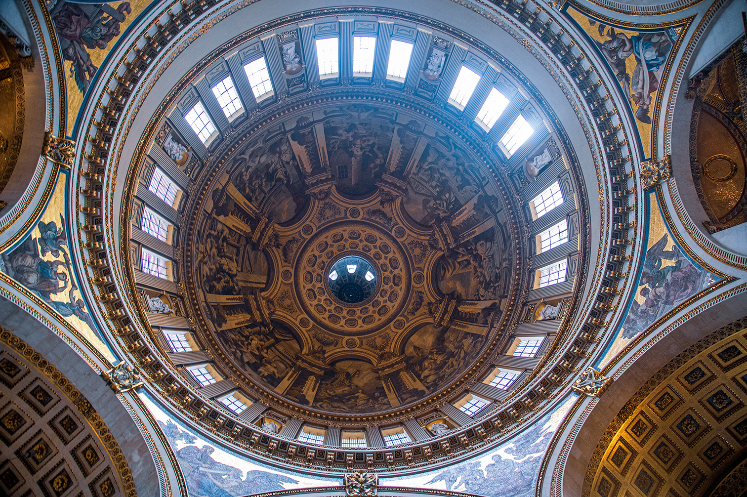The image depicts the ornate interior dome of a grand architectural structure, likely a historical or religious building. The dome is richly decorated with intricate frescoes, detailed carvings, and gold accents. The design features multiple levels of windows that allow natural light to illuminate the interior. The frescoes include various figures and scenes, adding to the grandeur and artistic value of the dome. The overall impression is one of opulence and meticulous craftsmanship.