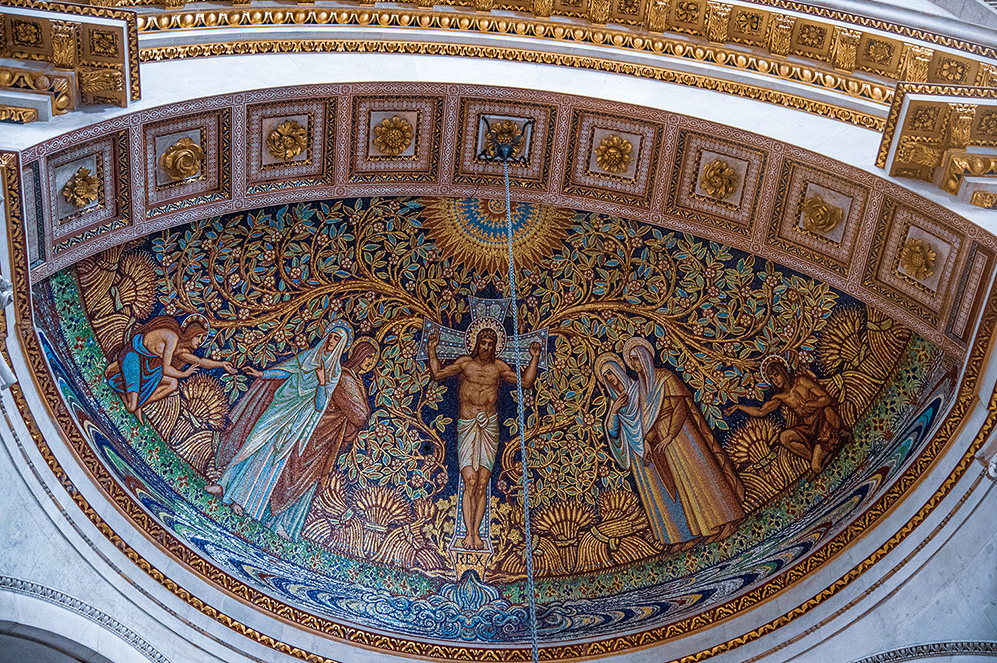 The image depicts an ornate, semi-circular mosaic set within an intricately detailed architectural frame. The mosaic features a central figure, likely a religious or mythological character, surrounded by various other figures in elaborate attire. The background is richly decorated with floral and vine motifs, and the overall composition is framed by gold and patterned borders