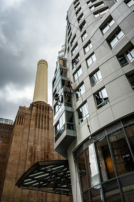 The image shows a modern building with a unique architectural design, featuring a curved facade and numerous windows. Adjacent to it is an older, industrial structure with a tall, cylindrical chimney. The sky above is overcast, adding a dramatic effect to the scene. The juxtaposition of the old and new buildings highlights the contrast between different architectural eras.