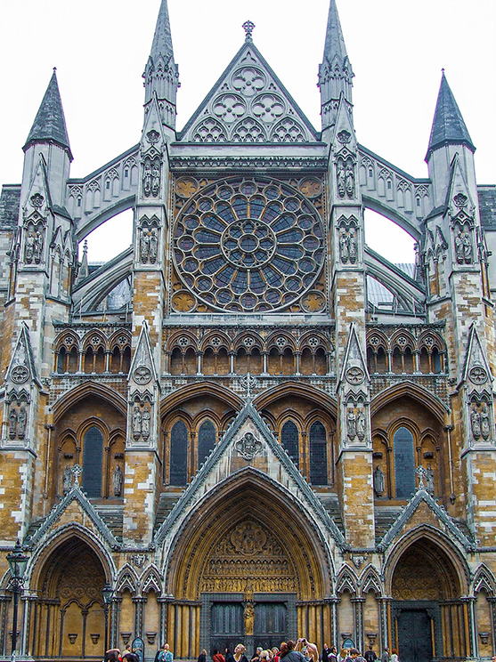 The image depicts the intricate and grand facade of Westminster Abbey, a large Gothic church in London. The structure features pointed spires, detailed stone carvings, and a prominent rose window. The entrance is framed by ornate arches and statues, with a crowd of people gathered in front, highlighting its significance as a historical and cultural landmark.