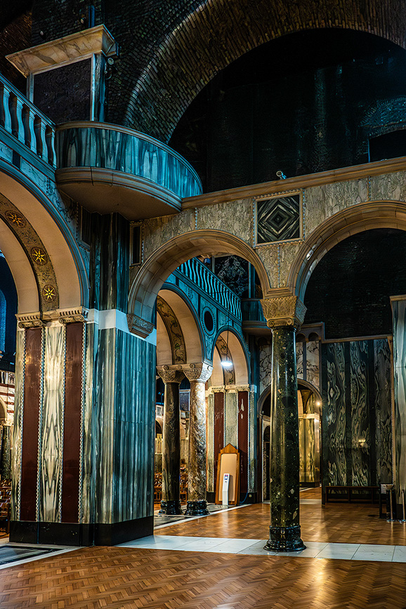 The image depicts an ornate interior space with intricate architectural details, including arched doorways, detailed columns, and a balcony with a curved railing. The walls and ceiling are adorned with rich, decorative patterns and textures, creating a luxurious and historical ambiance.